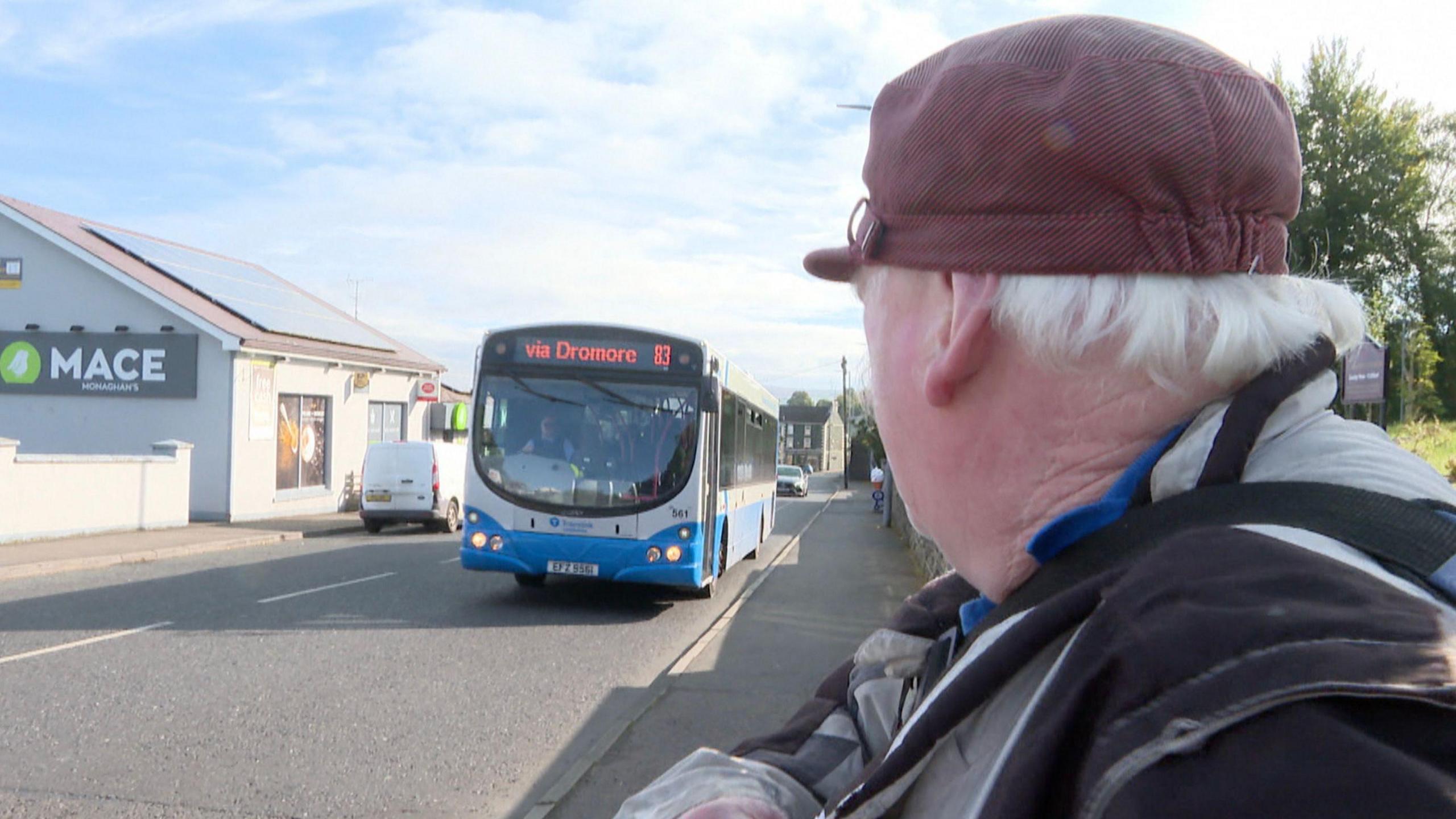 Man wearing a red hat with his back to the camera, looking towards an oncoming Ulsterbus which is travelling towards Dromore 