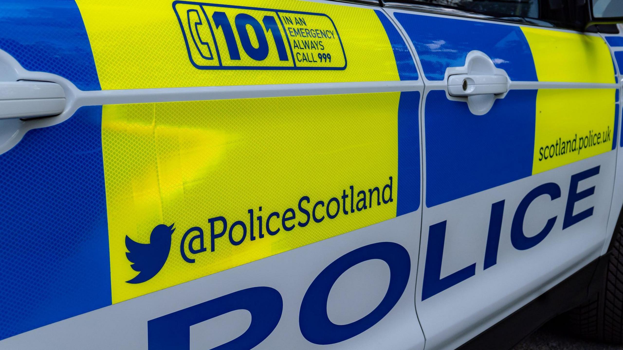 A close up of a police car. The vehicle is decorated with blocks of yellow, blue and white colours and has information on how the public can contact police and follow Police Scotland on social media.