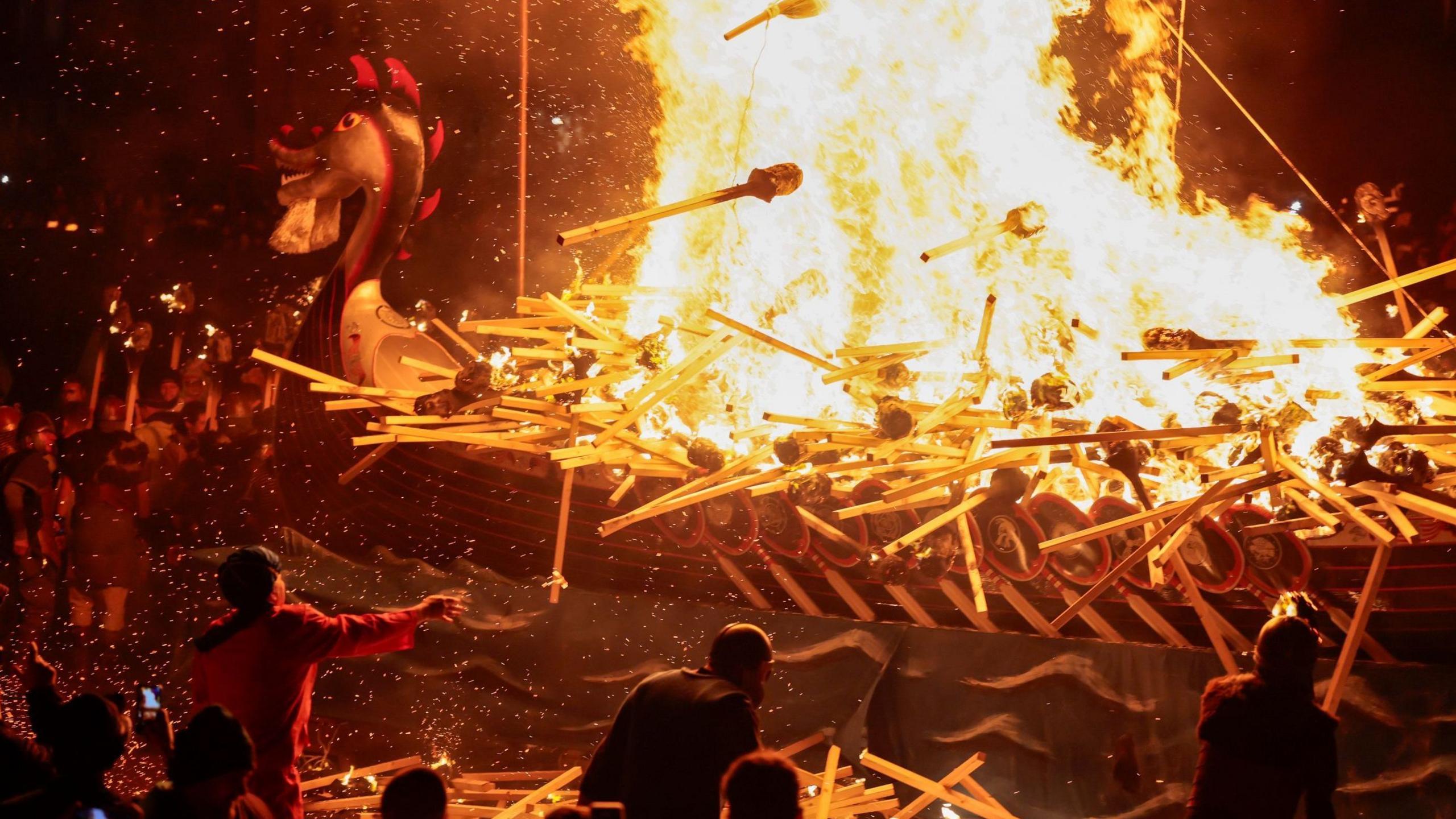 Members of the festival throw burning torches on to the replica ship, which is ablaze.