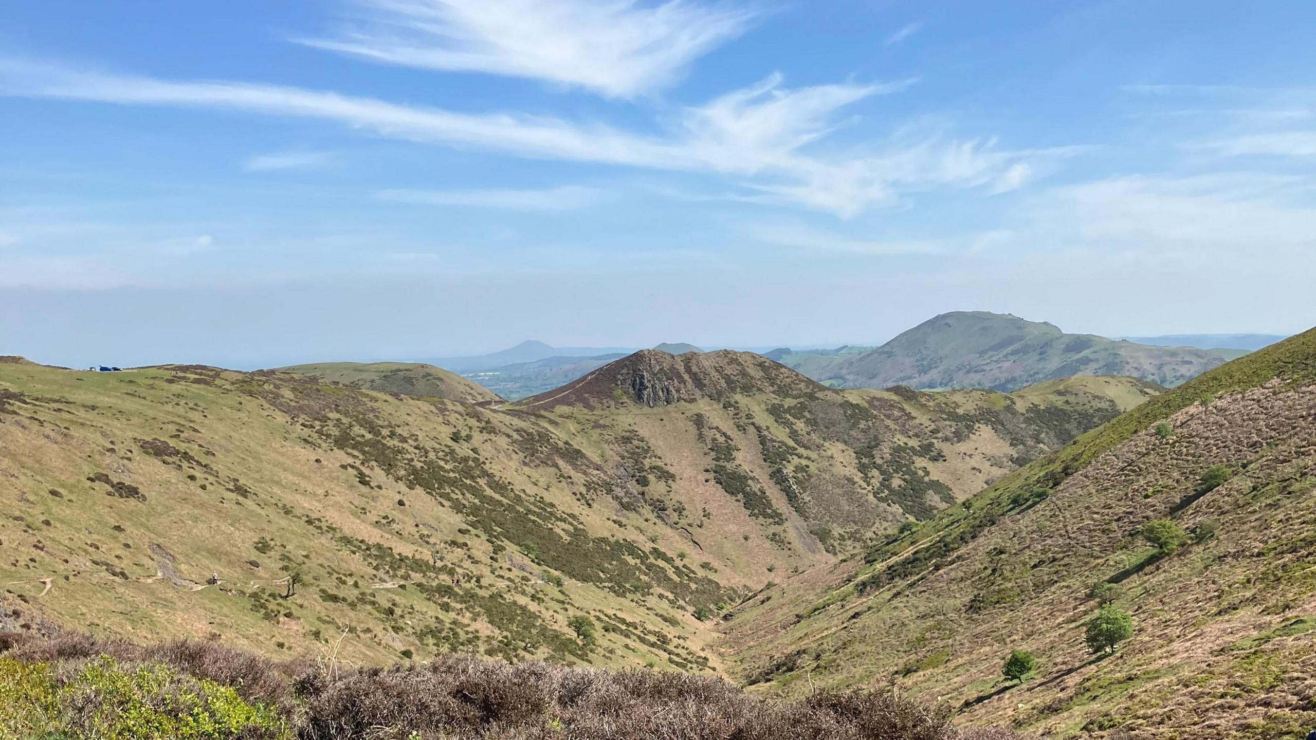 Blue sky interspersed with clouds over dry, hilly ground 