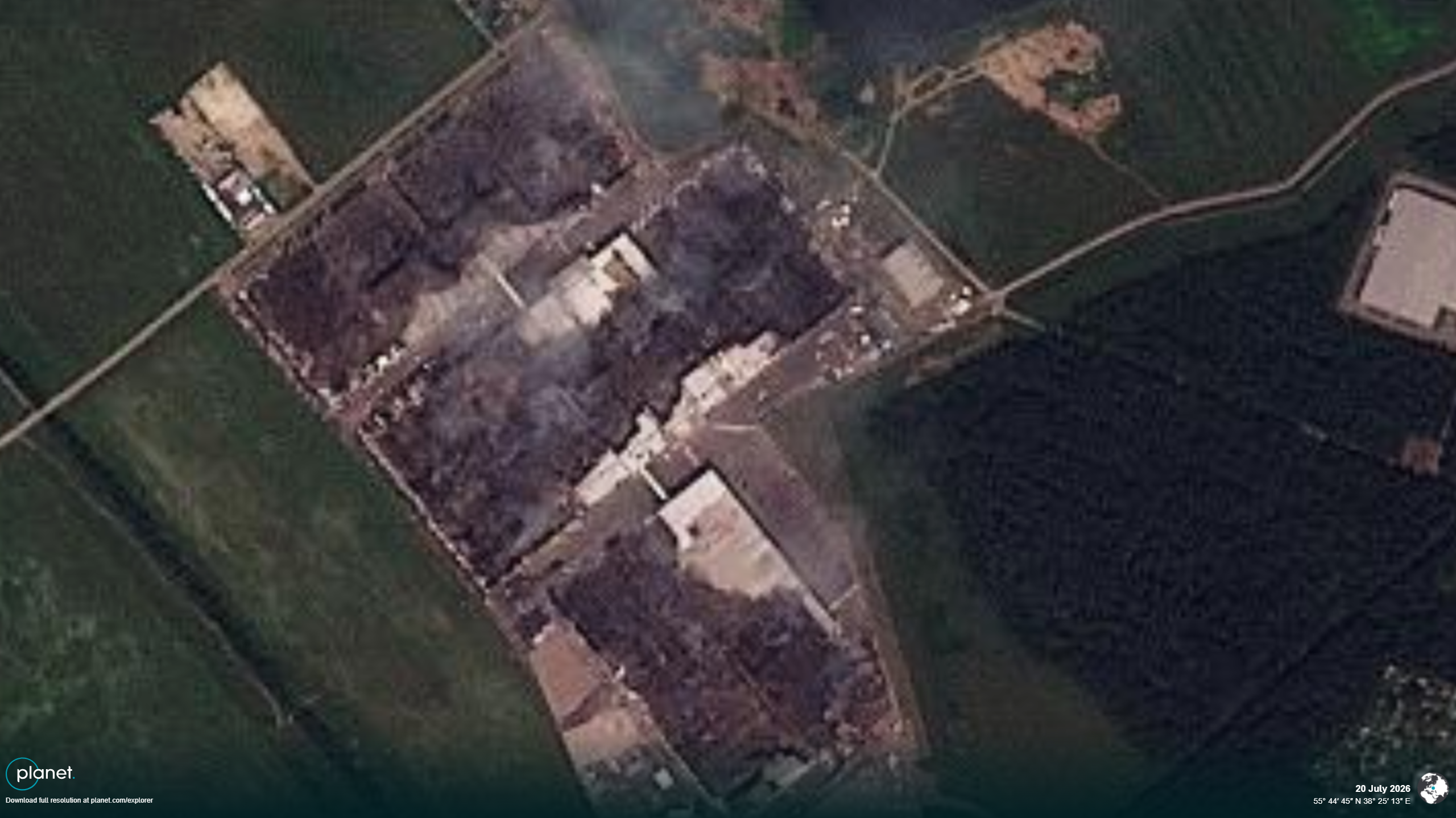 A satellite image shows burned buildings surrounded by roads and green fields