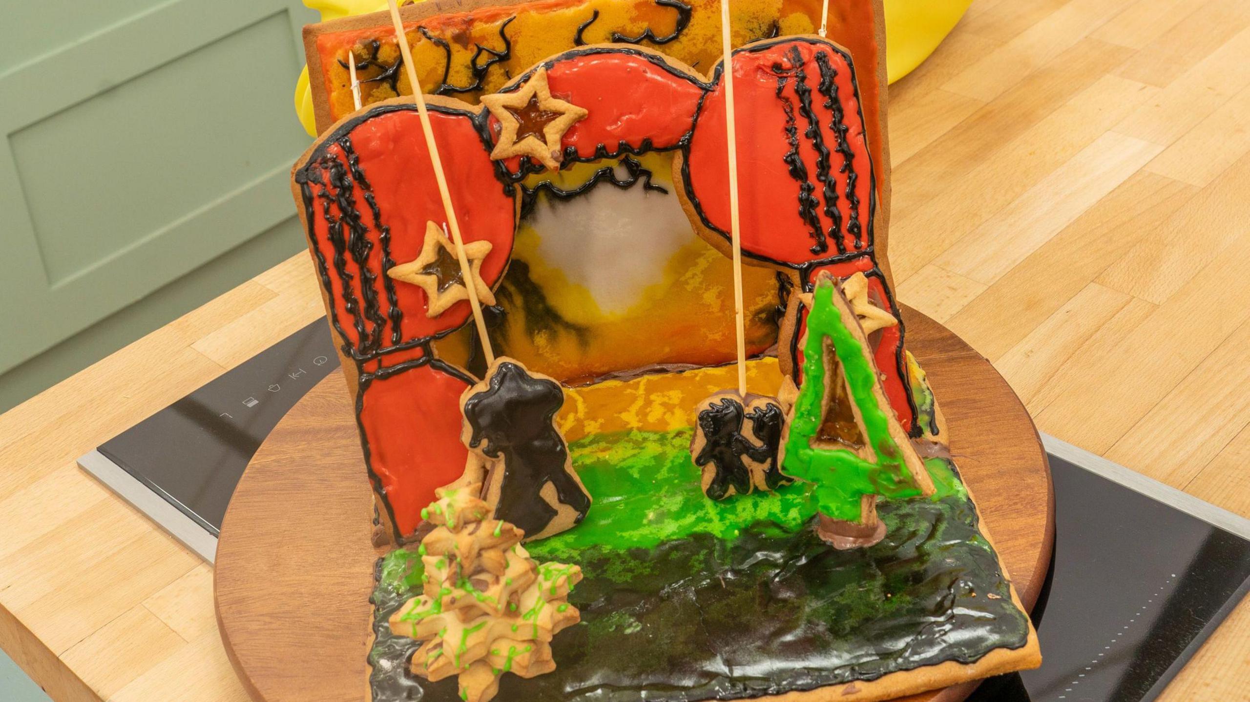 A theatre stage made out of iced biscuit, with orange curtains decorated with stars and a green tree, on a circular wooden board about the size of a dinner plate