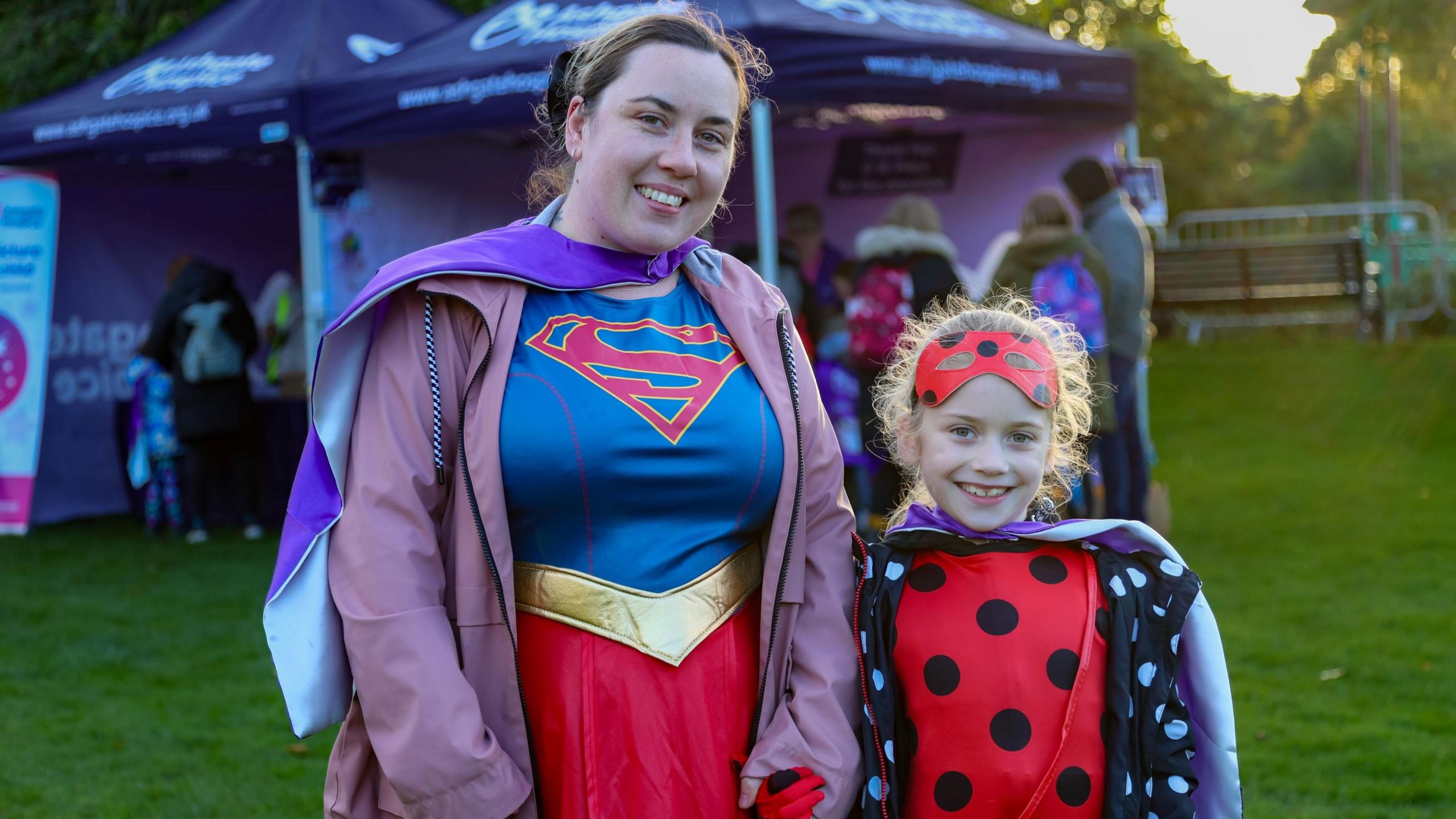 Abbie, who is standing on the left, holding hands with her daughter Darcy-Grace and they are both wearing superhero costumes