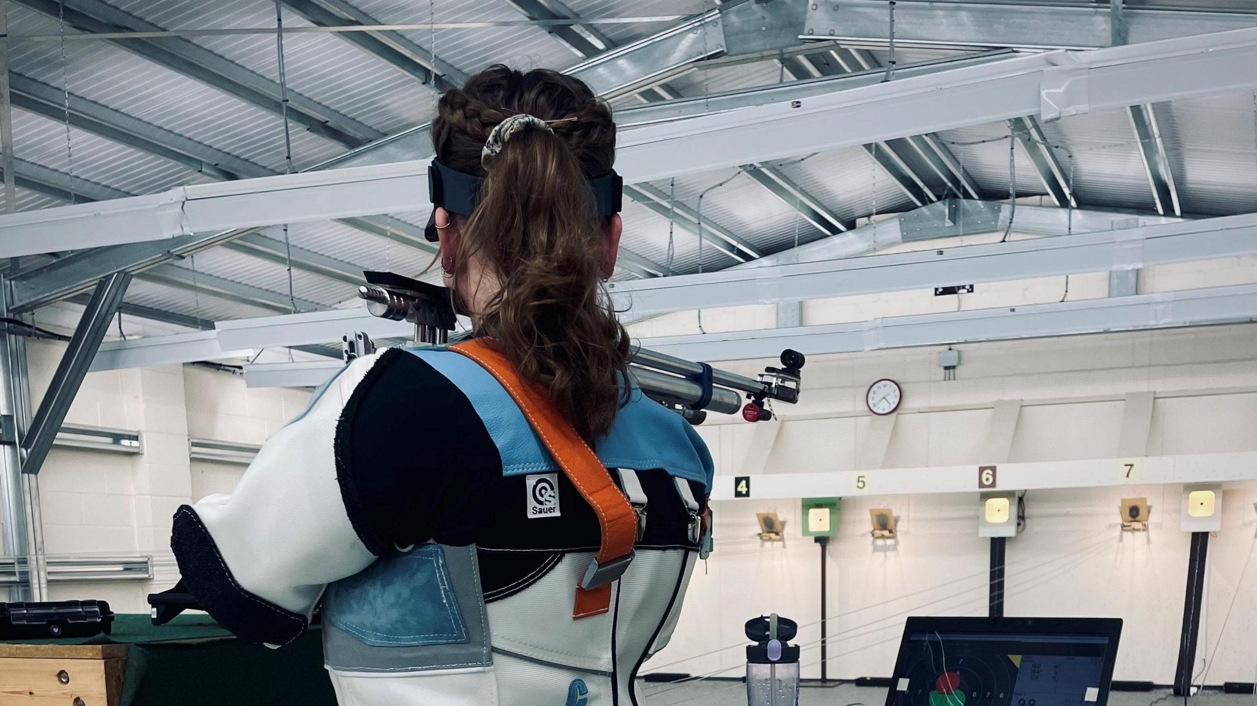 A woman has her back to the camera and is holding a gun, aiming at a target