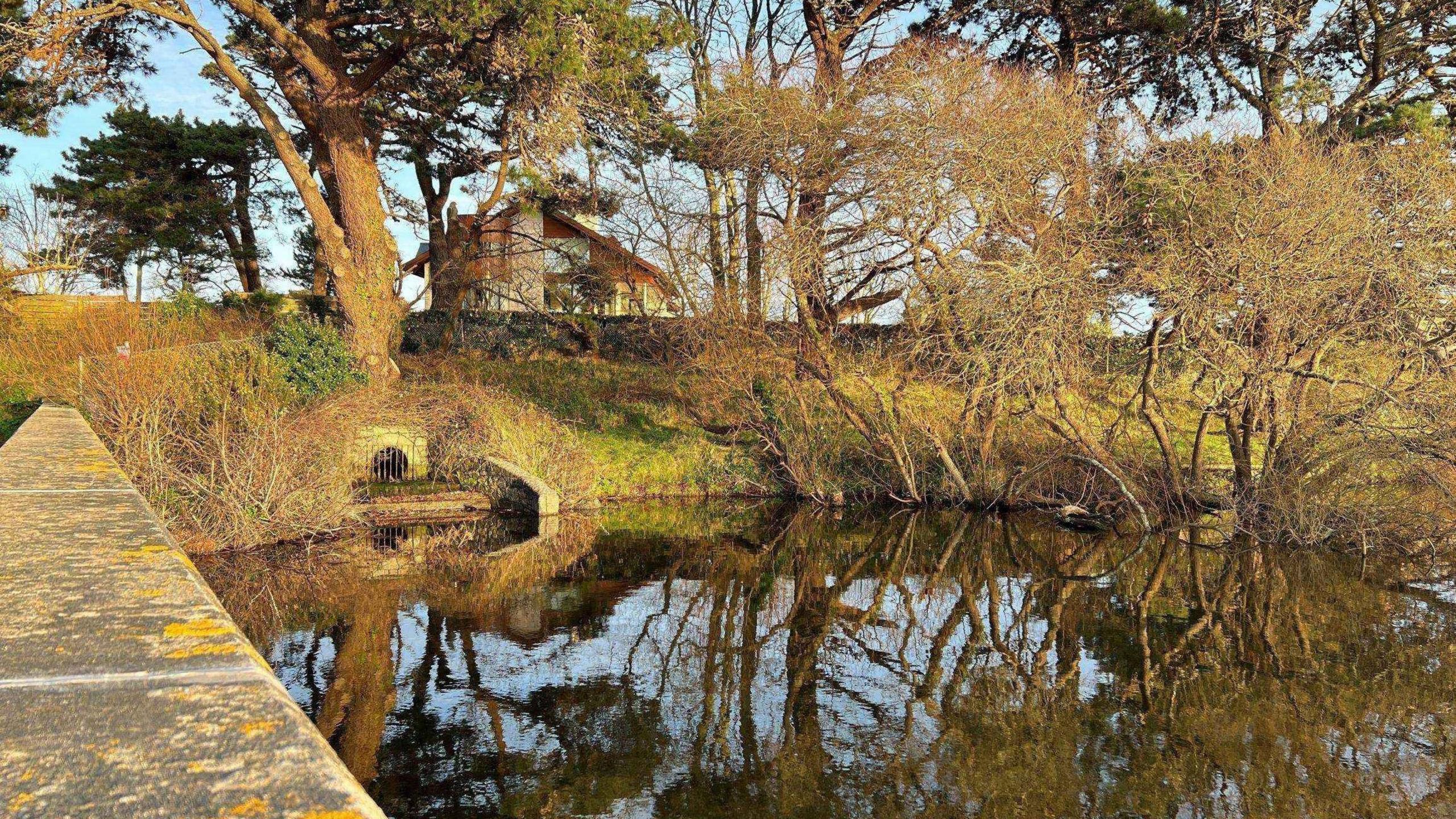 Photo of the reservoir in Guernsey. The sun is shining down on the water and there are blue skies.