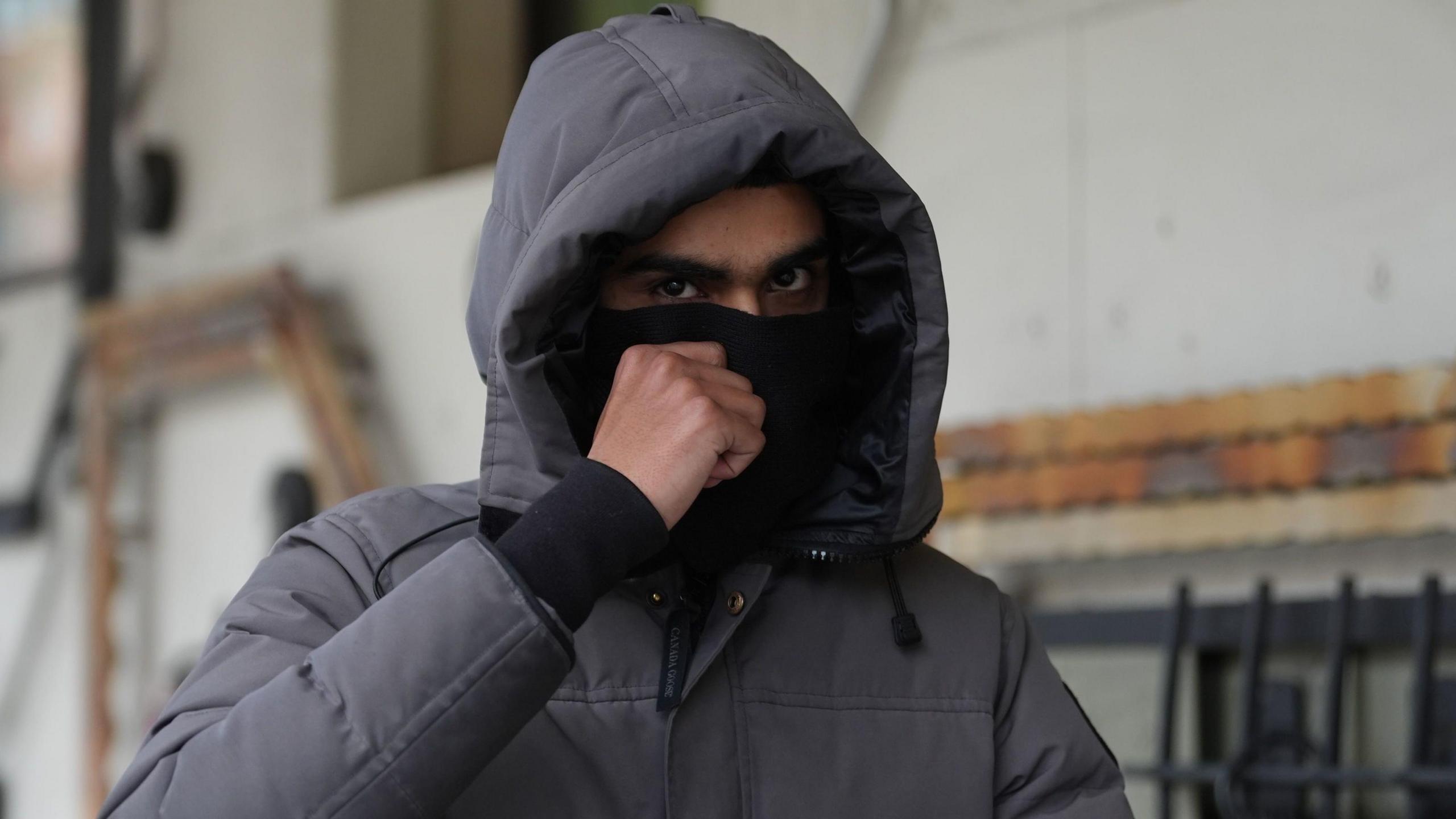 Imran Chowdhury outside court wearing a coat with the hood up and covering his face with a black material so only his eyes can be seen.