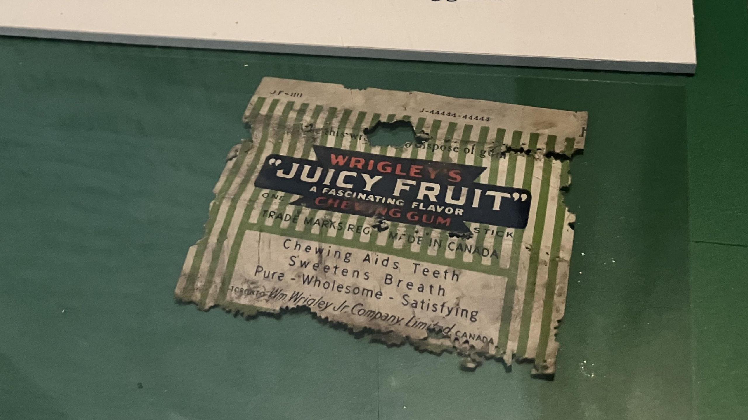 An old, battered chewing gum wrapper for Wrigley's Juicy Fruit with green and white stripes.
