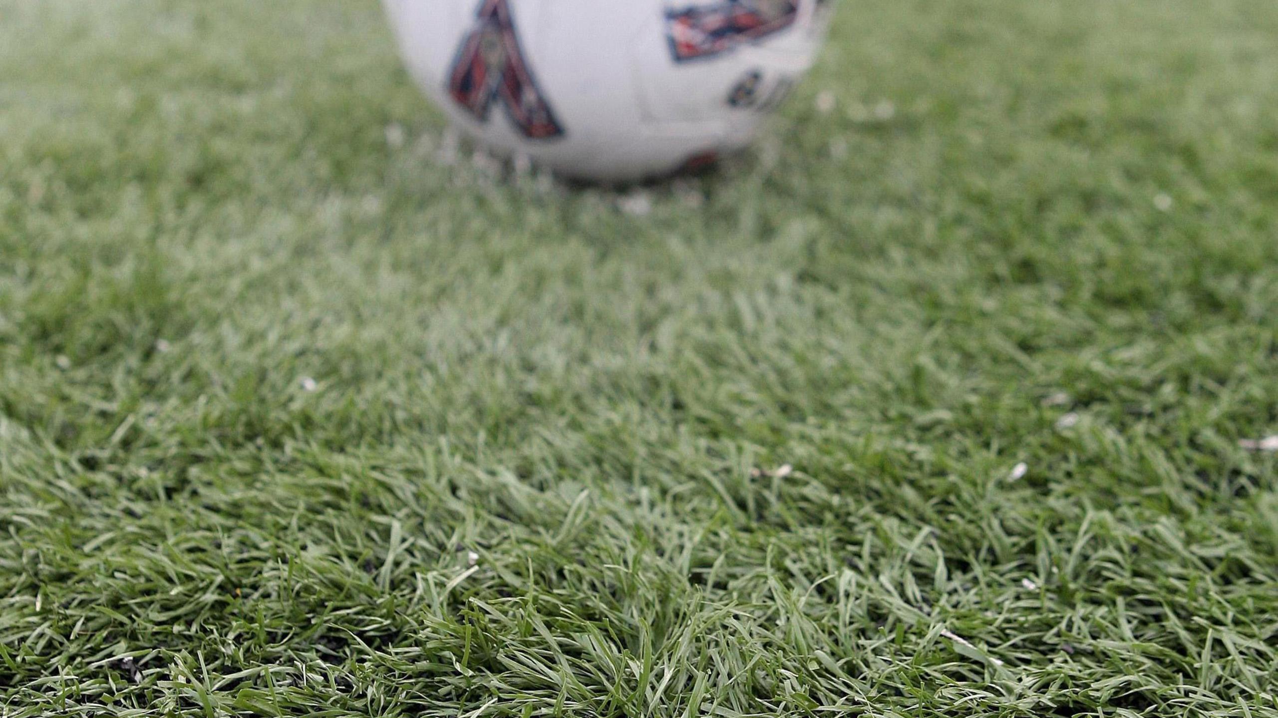 An artificial playing field with a football in the background.