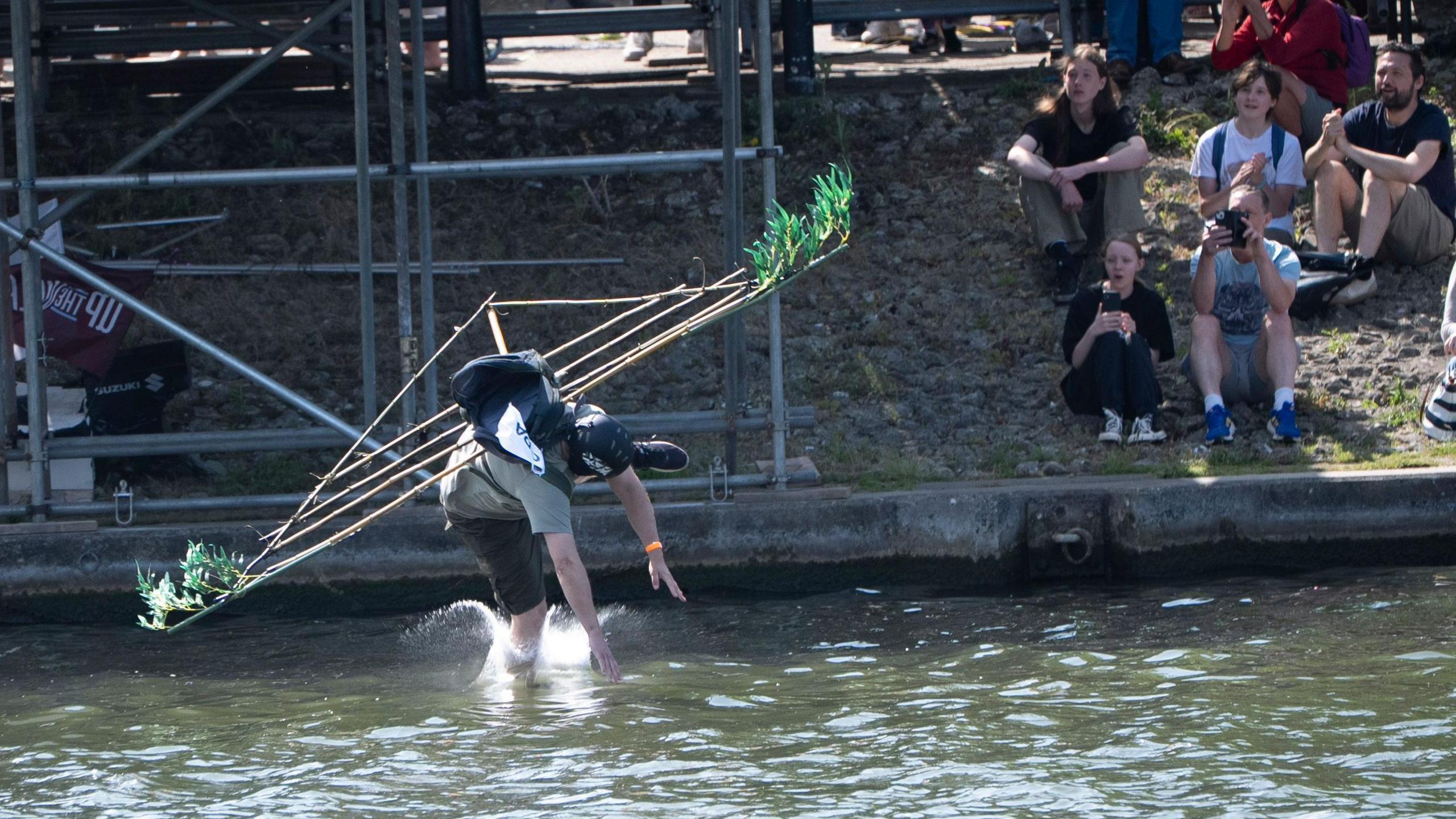 A man falling to Bristol Harbour wearing a flimsy-looking construction of bamboo canes and a few leaves