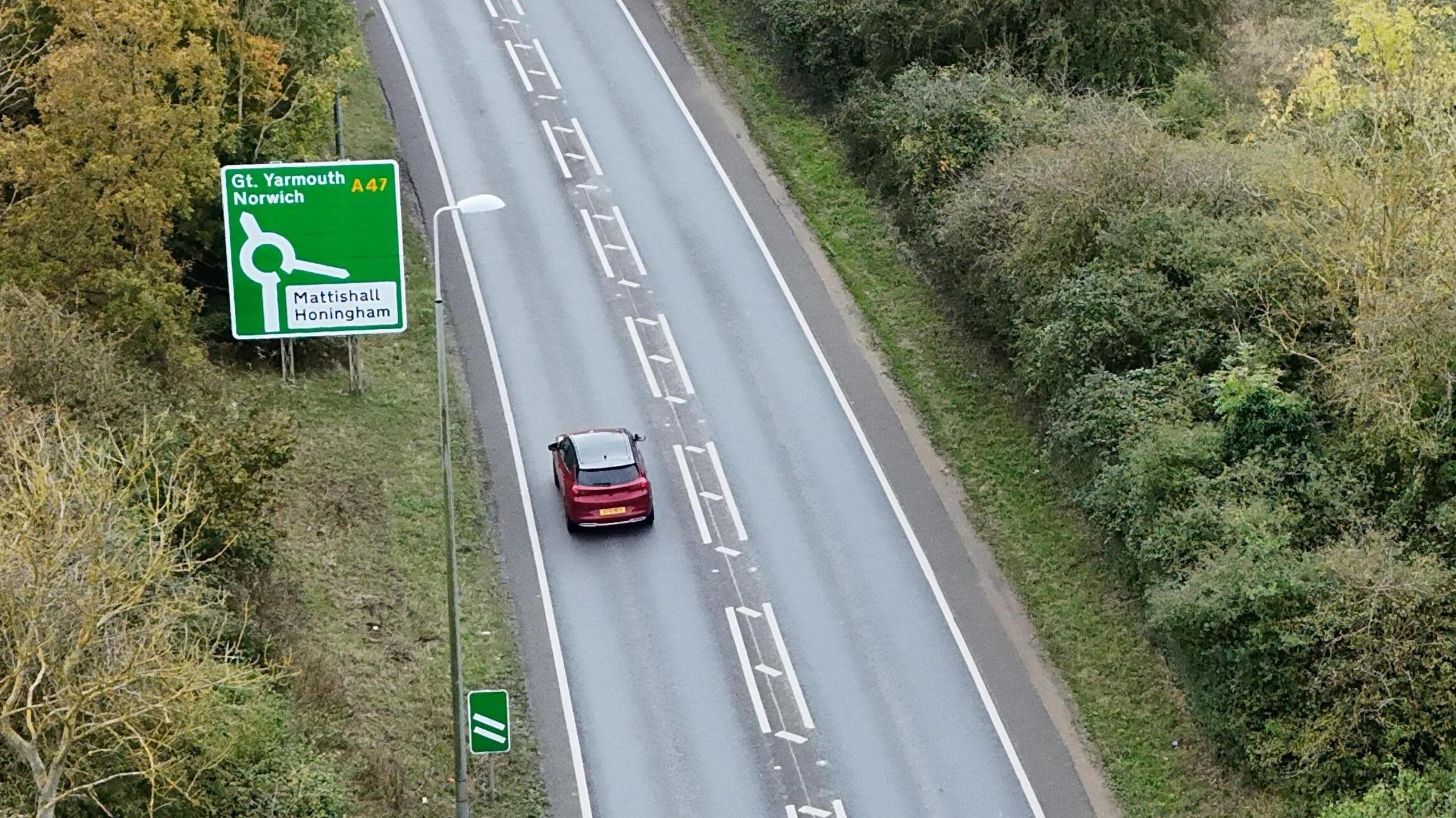 An aerial view of the A47 road leading to Costessey, just outside of Norwich. A green road sign points to Matishall and Honingham and upwards to Great Yarmouth and Norwich.