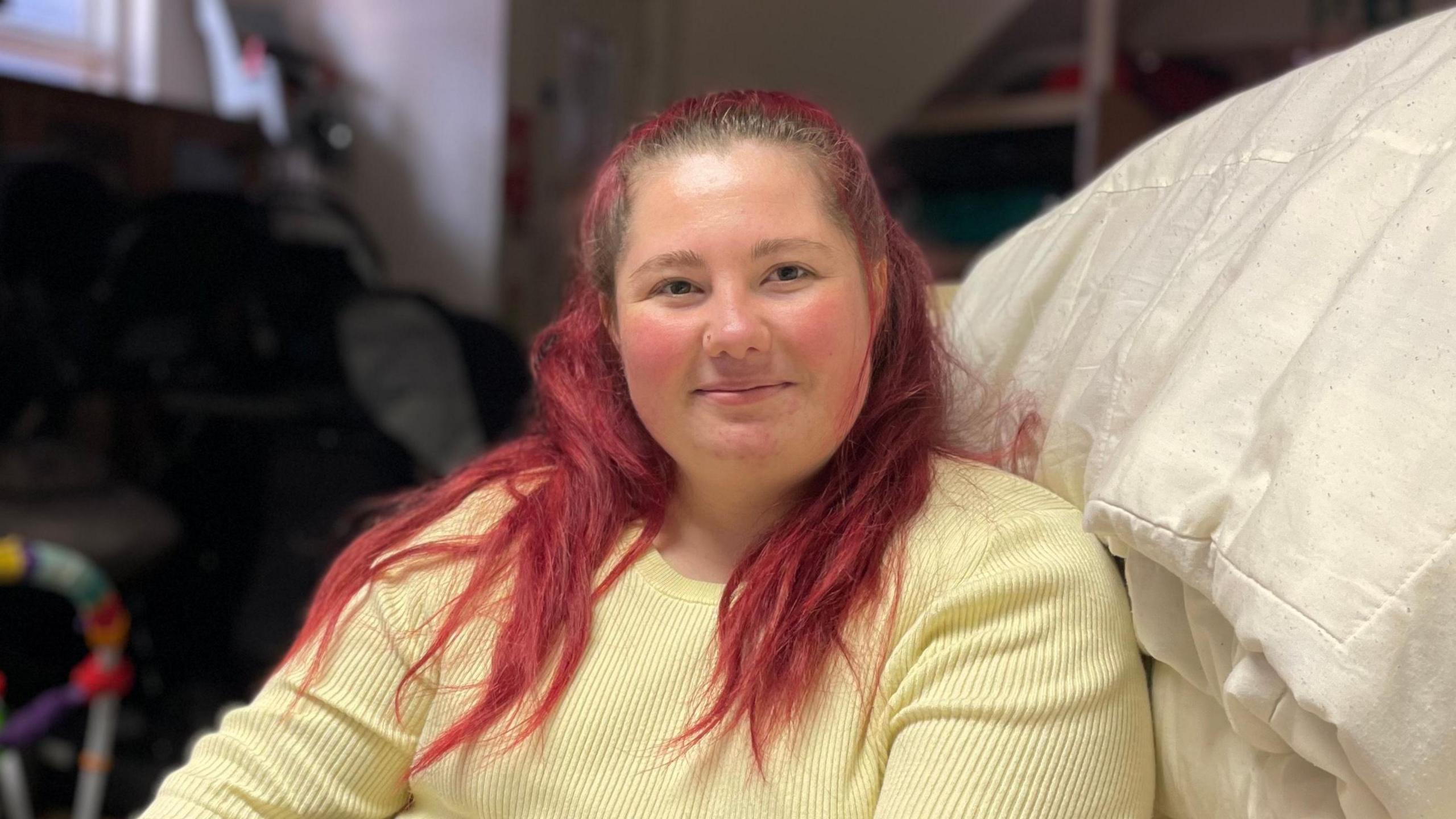 Ellie, with long red hair and a yellow jumper, sitting on a white sofa.