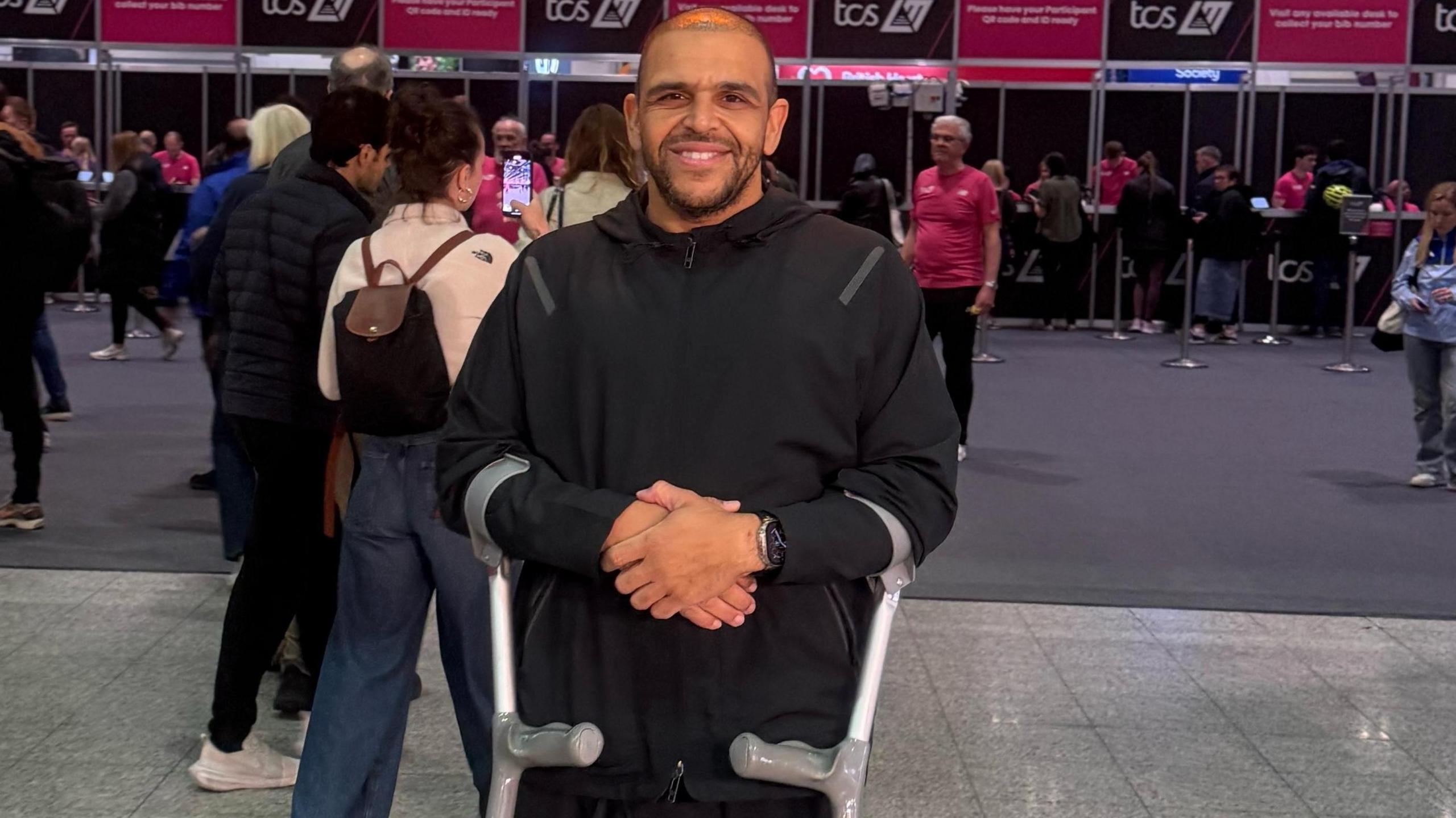 Darren Awol, wearing black hoodie, smiles at the ExCel Centre with arm crutches