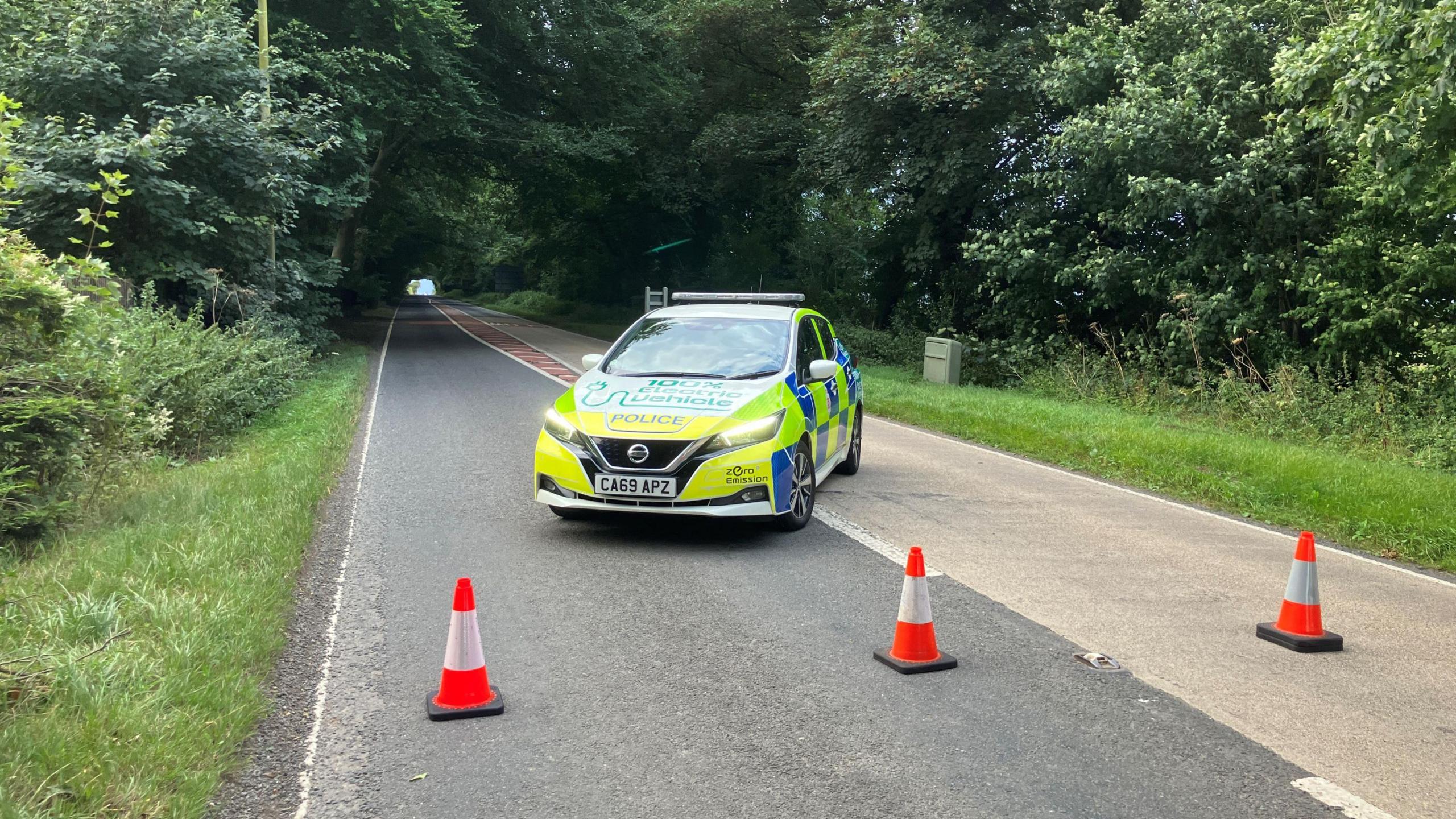 A police car parked behind some traffic cones on a country road