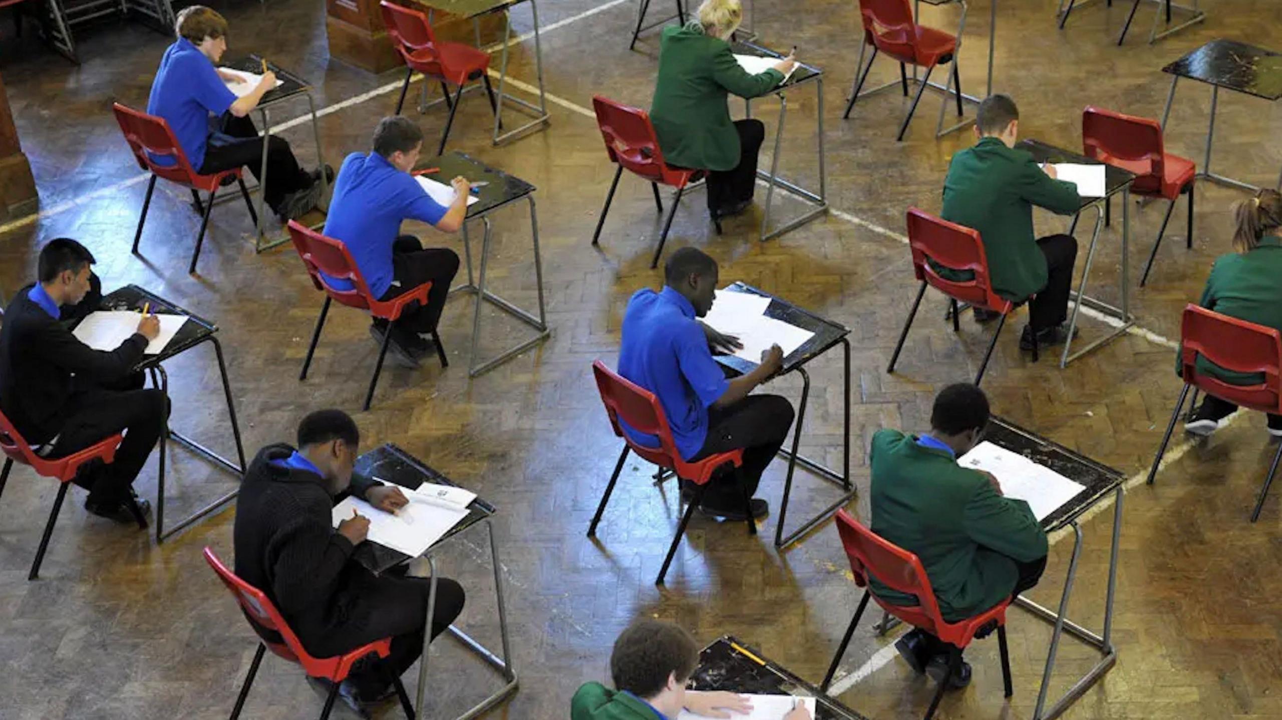 Children in school uniform sat in rows on individual desks and chairs sitting an examination.