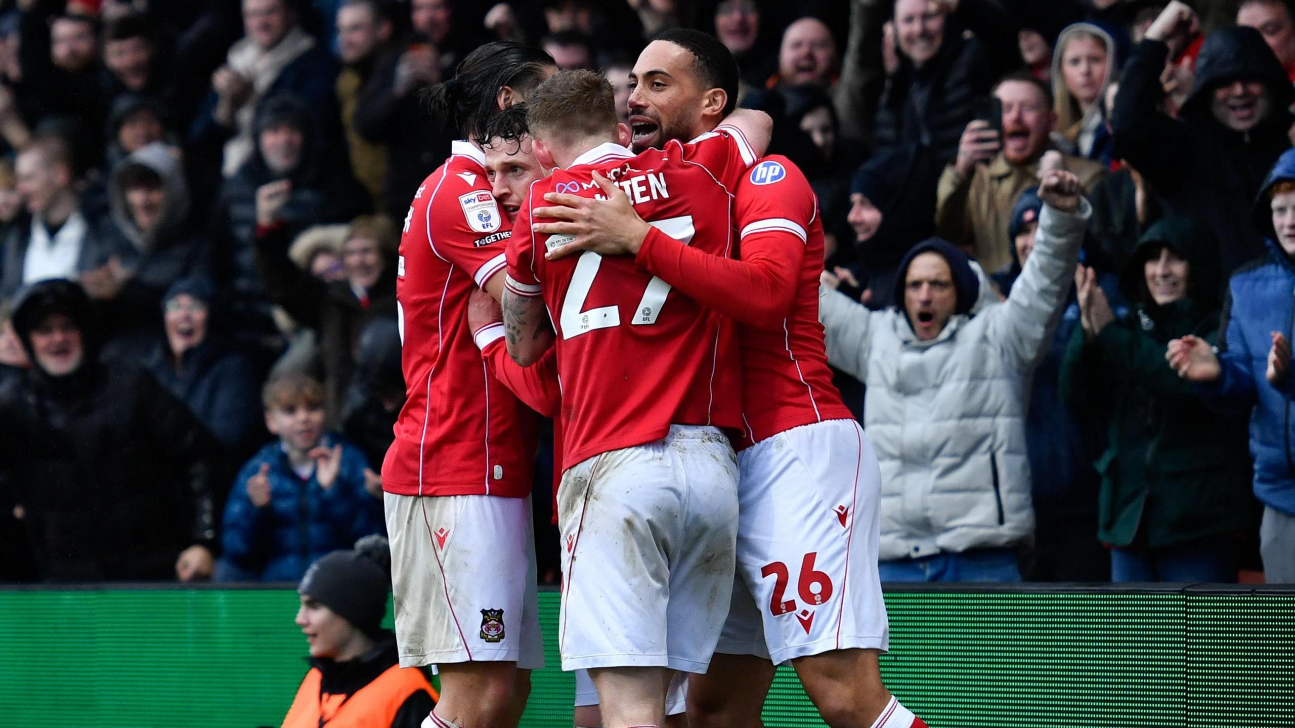 Wrexham players celebrate in their red tops and white shorts after scoring a goal 