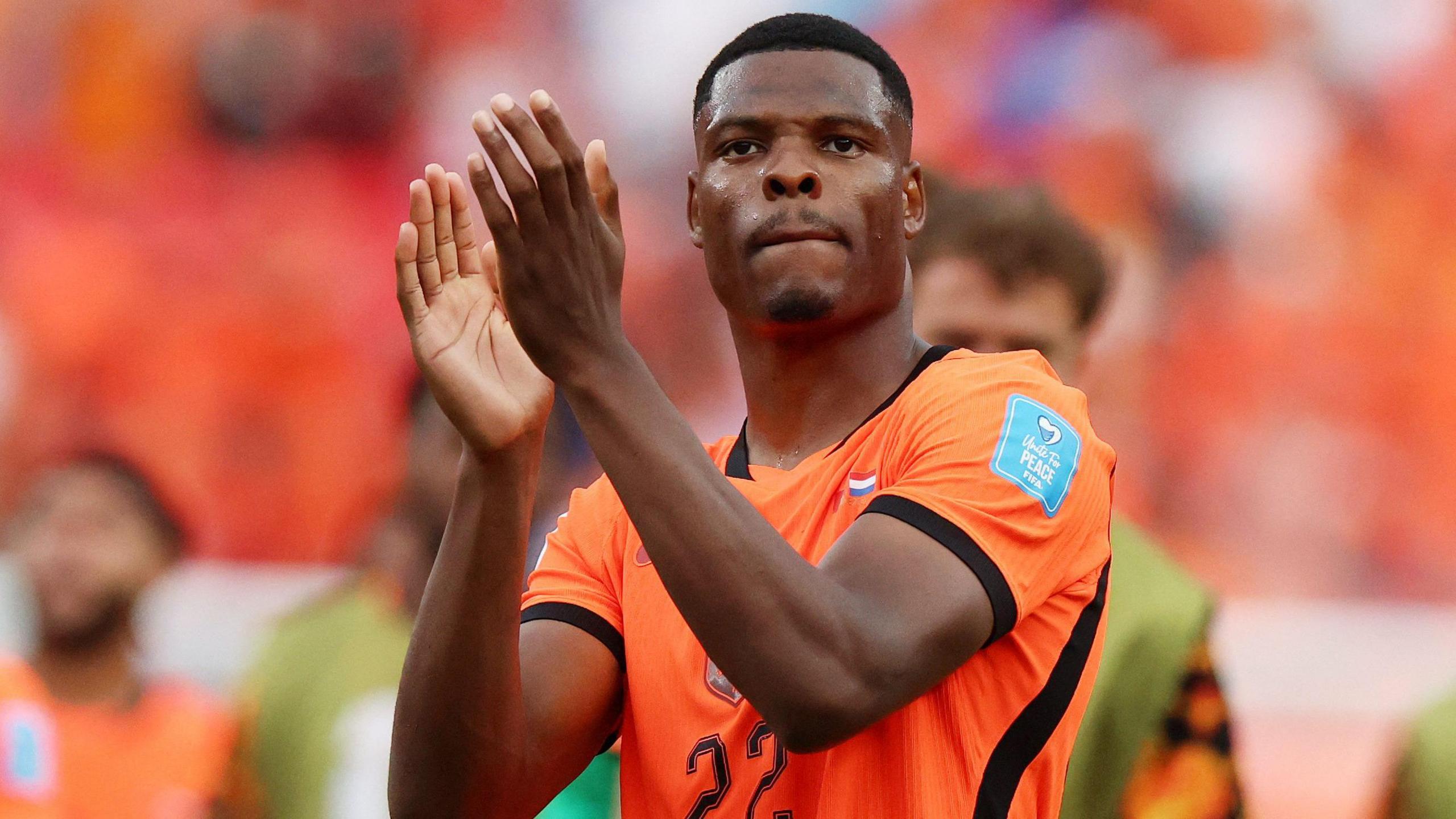 Footballer Denzel Dumfries claps his hands at full time in a bright orange strip of the Netherlands with the number 22 on the front