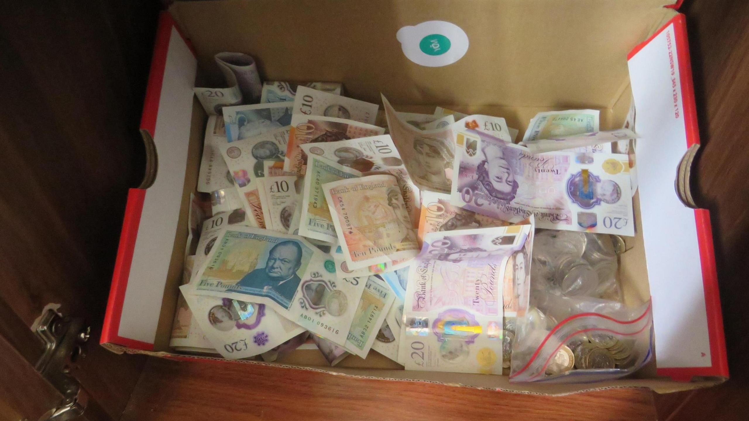 A cardboard box with a pile of pound notes and coins inside.