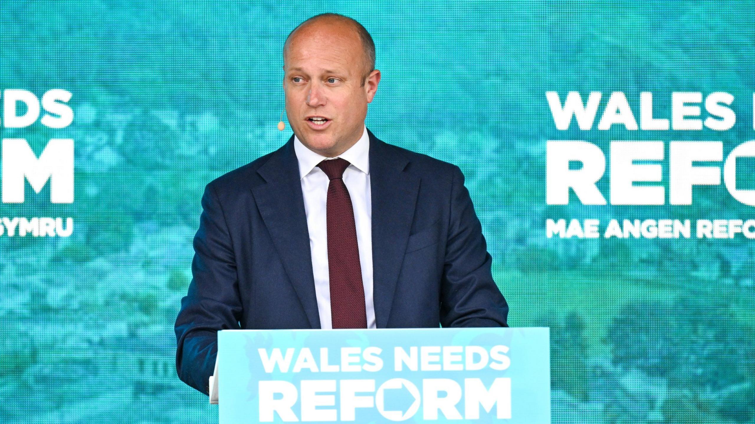Dan Thomas yn areithio gyda logo Reform o'i flaen