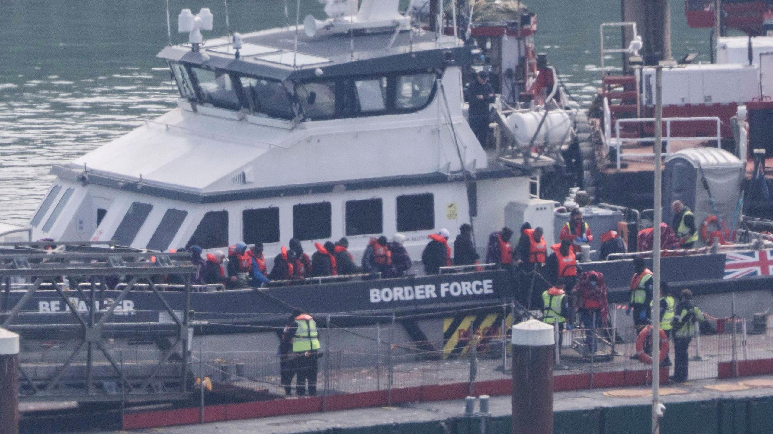 Migrants wearing orange life jackets leave a Border Force boat at a dock in Dover