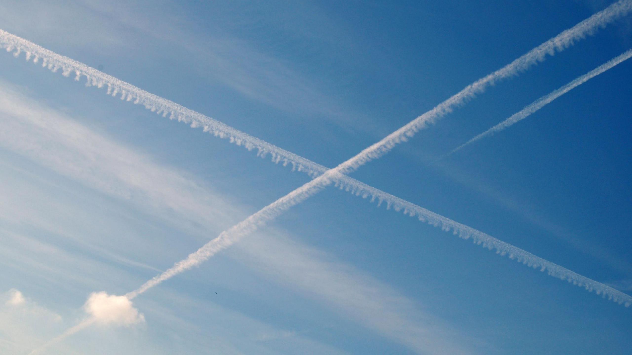 Two contrails, white plumes of cloud caused by aircraft, crossing in mid-air against a blue sky