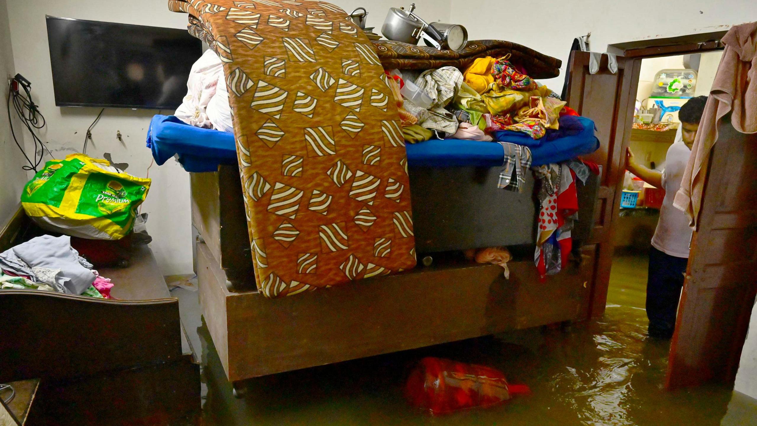 Sofa, bed and other furniture submerged in water due to floods as a man stands at the gate and stares at his losses in Punjab, India.