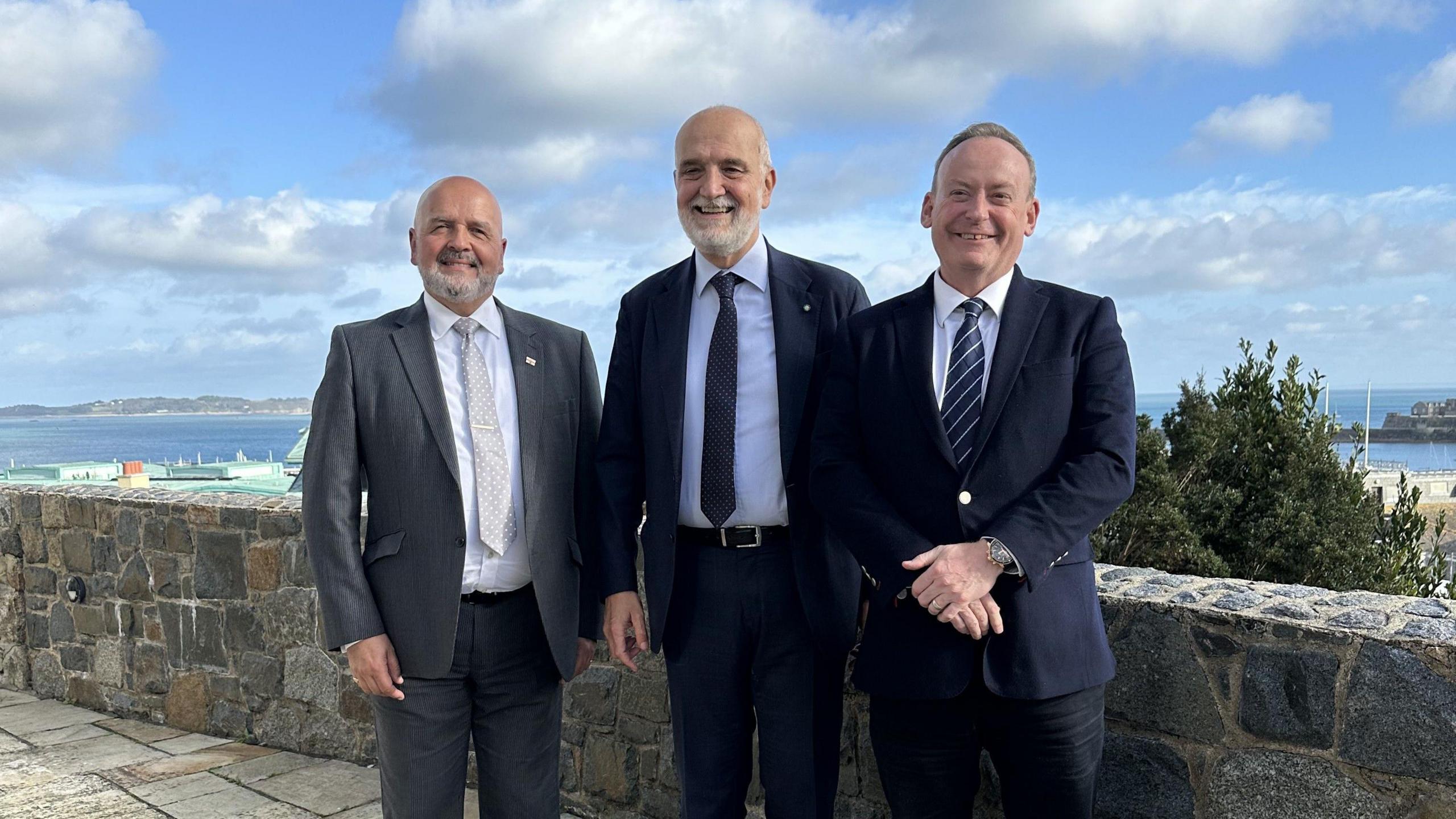 Three men in suits standing outside near a stone wall. In the middle is Ambassador Inigo Lambertini. Guernsey Chief Minister Lyndon Trott is on the right.