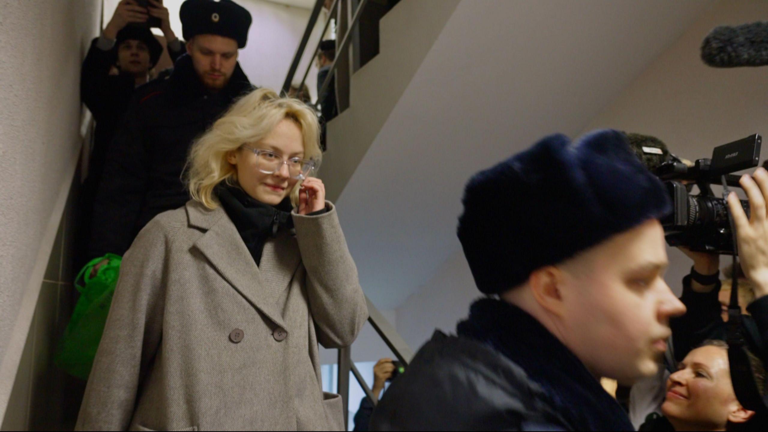 Diana Loginova walks down the stairs, surrounded by police and journalists, in a St Petersburg courthouse