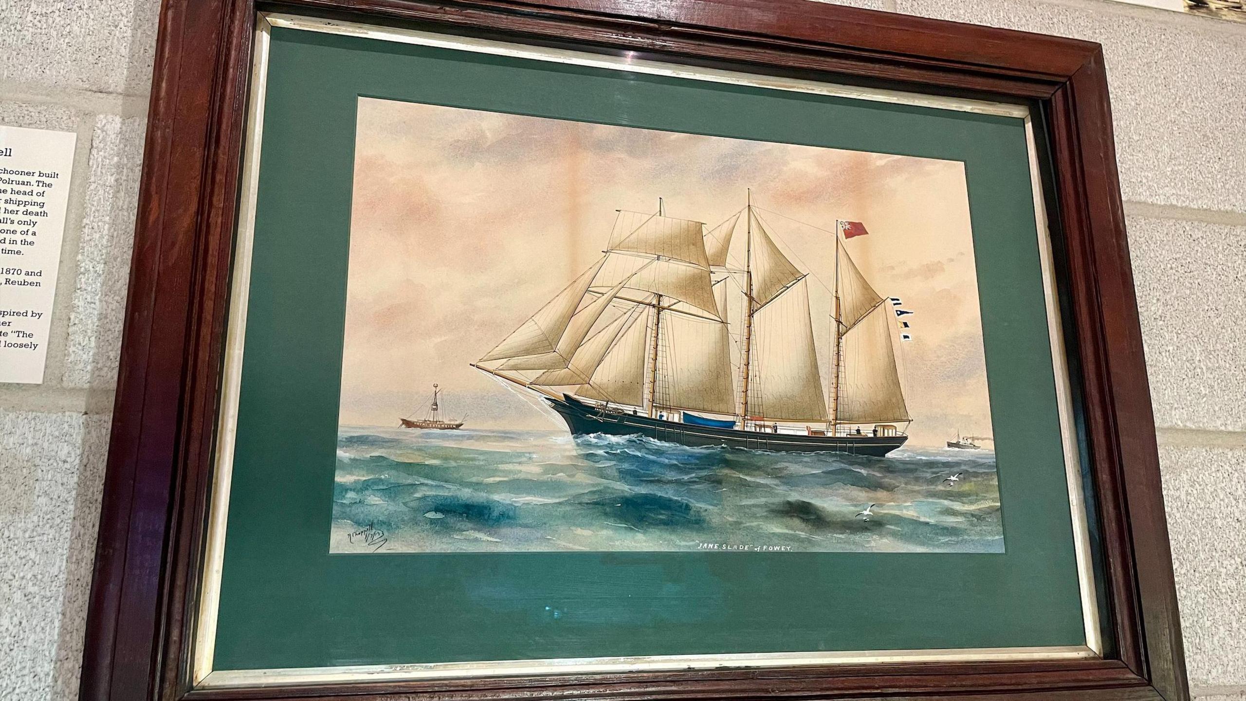 A painting in a wooden frame showing a boat at sea with white sails.