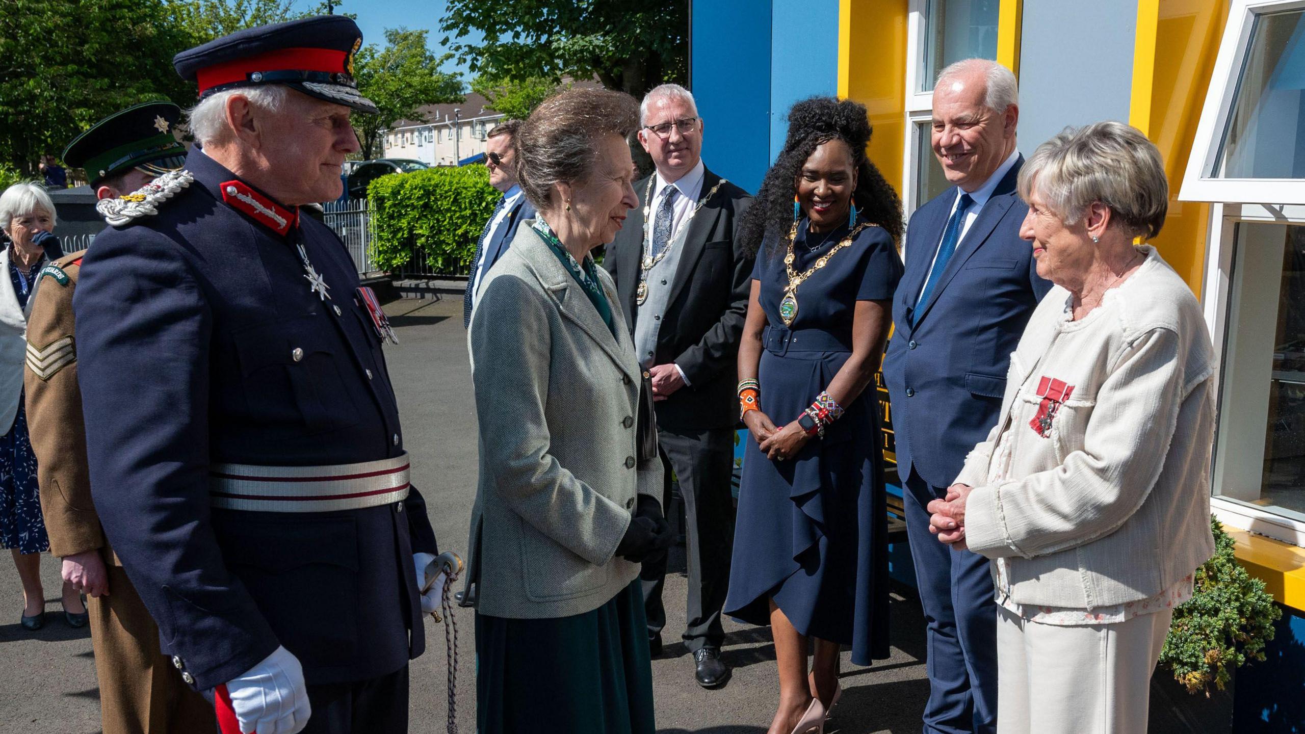 A man in military uniform, stands alongside a group of women during a royal visit to derry