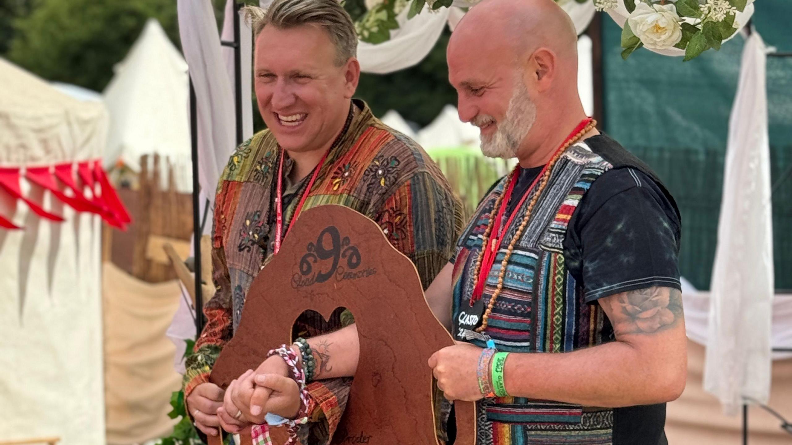 Two men with a heart-shaped wooden block having their hands tied in marriage