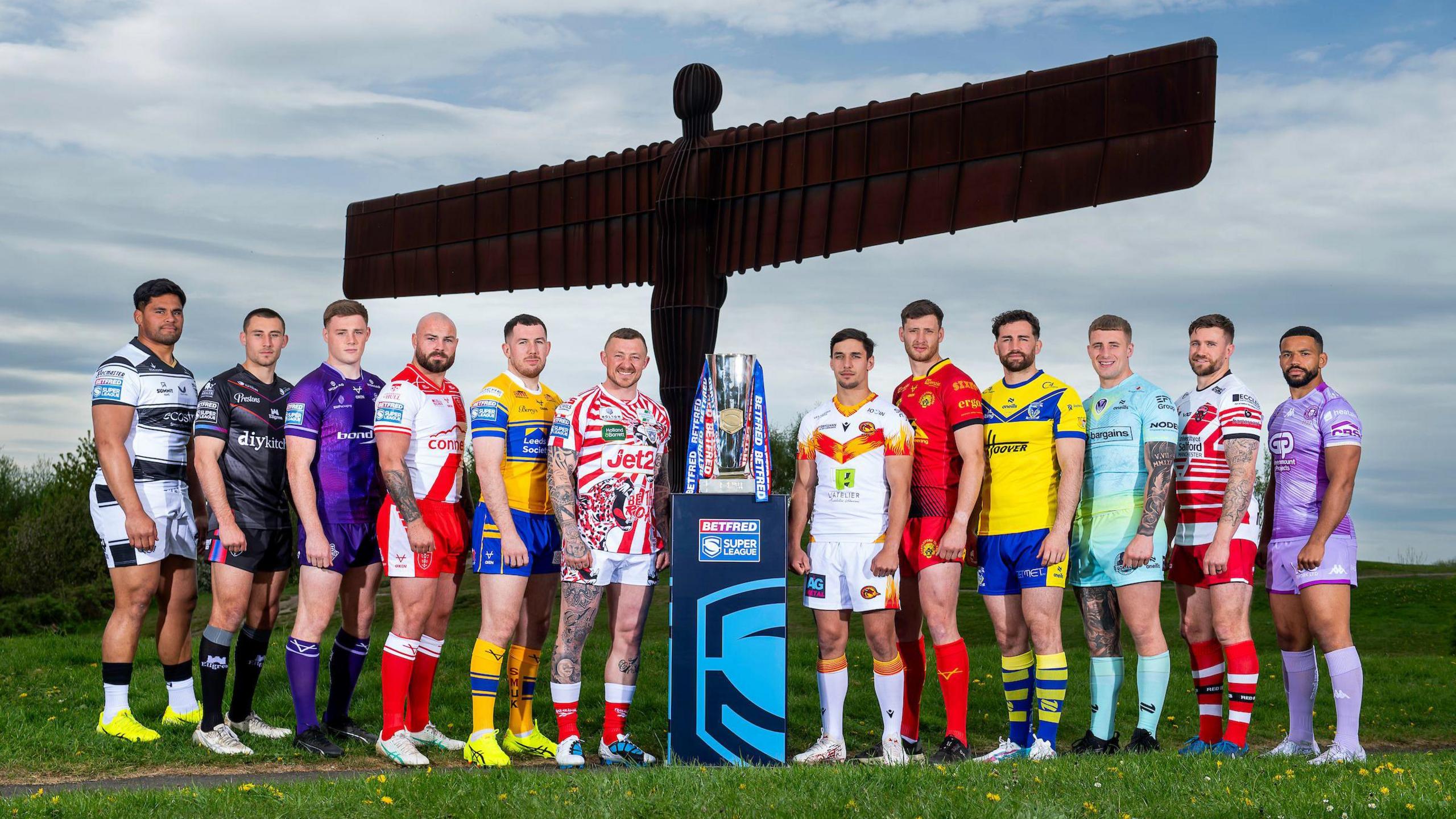 Herman Ese'ese, Oliver Pratt, Sam Halsall, Sam Luckley, Cameron Smith, Josh Charnley, Cesar Rouge, Sam Wood, Toby Kiung, Jake Wingfield, Ben Hellewell and Kruise Leeming stand aside the Super League trophy and in front of the Angel of the North