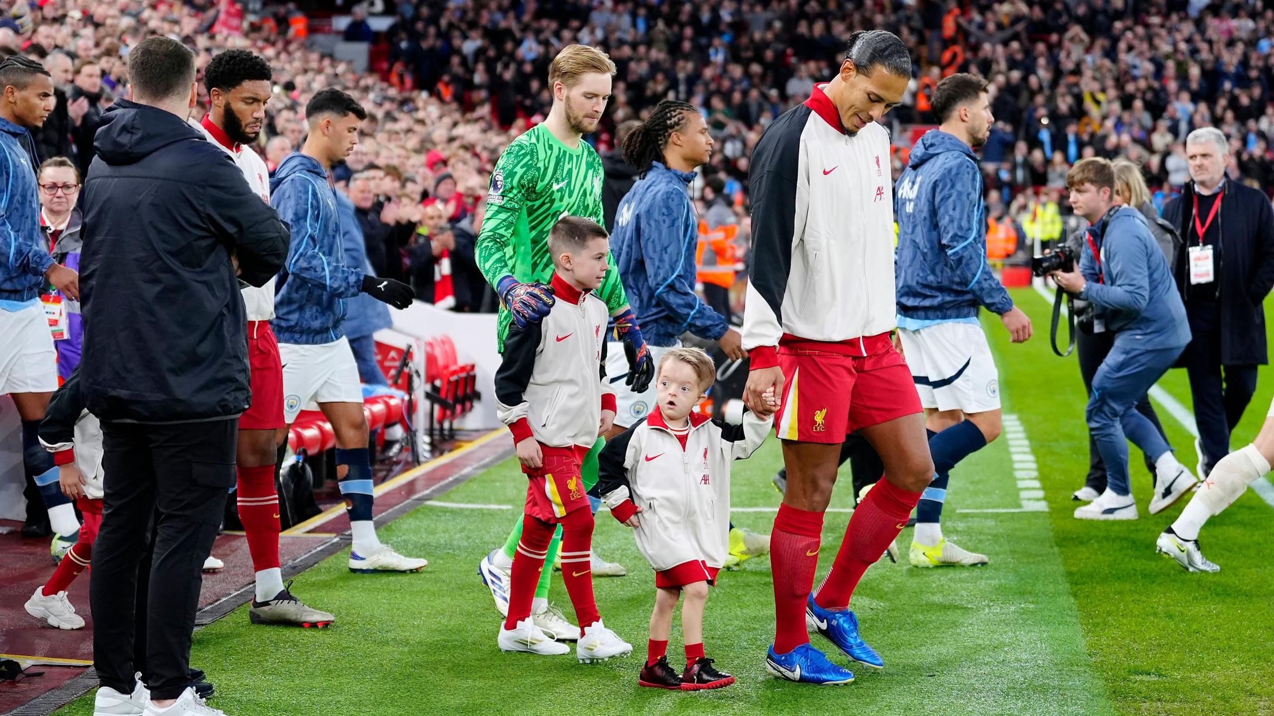 Virgil van Dijk holds Isaac's hand as they lead the Liverpool and Manchester City squads on to the pitch in front of packed stands at Anfield