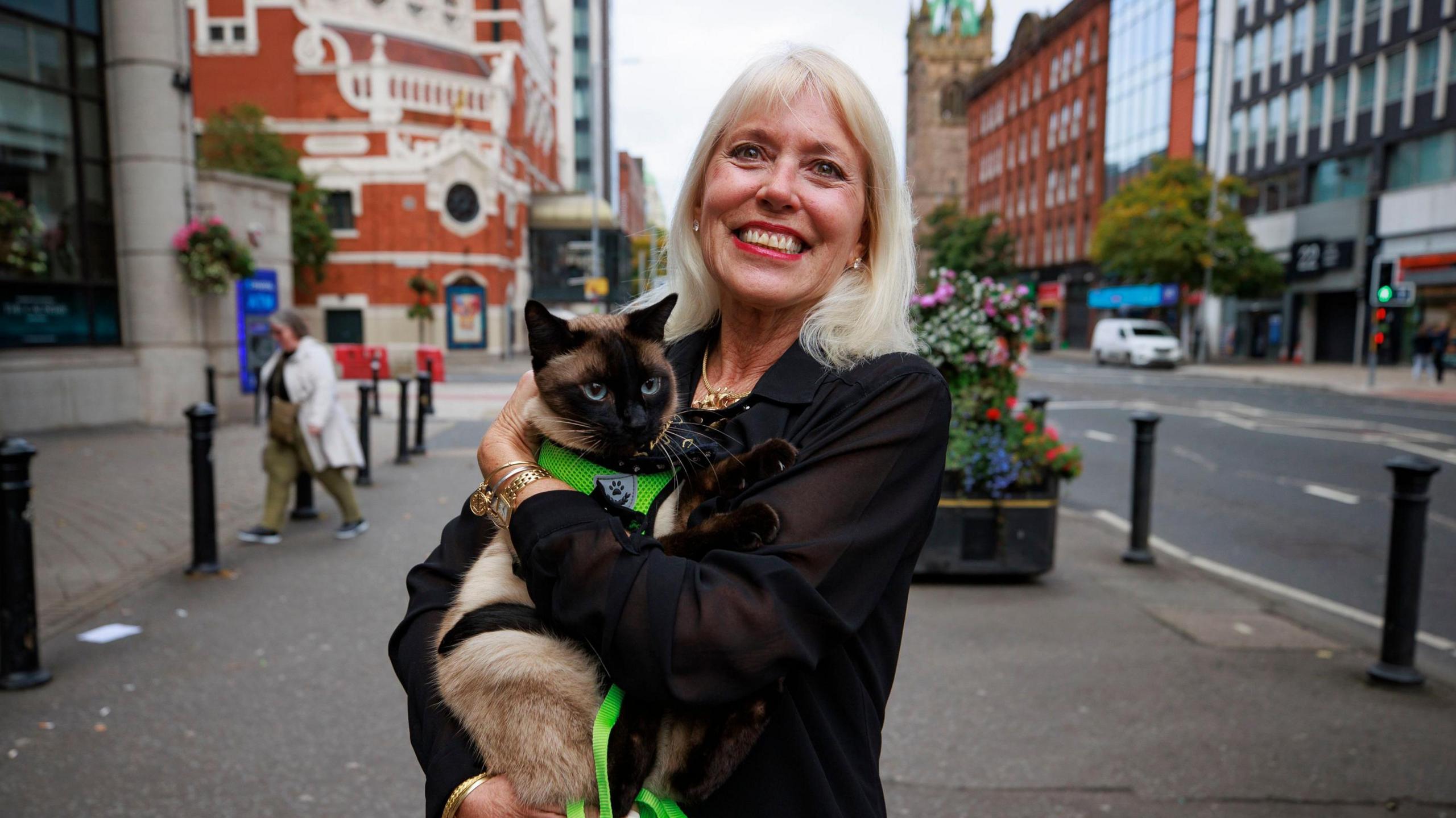 Holly Hennessy holding her Siamese cat Captain at the Europa Hotel in Belfast. Holly has blonde hair, wearing a black coat and smiling.