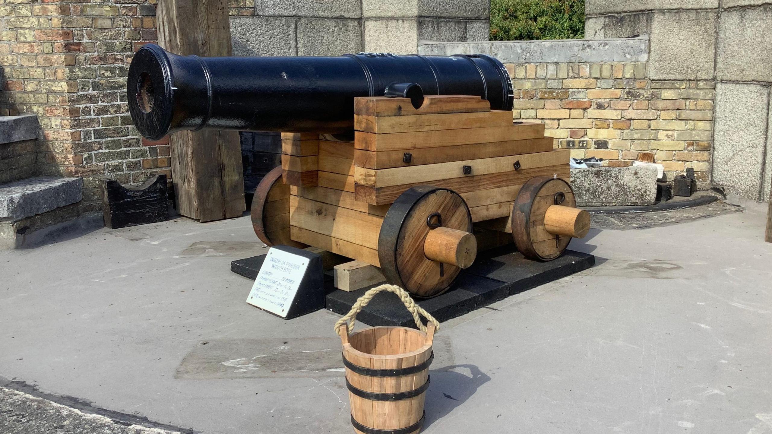 A canon and wooden carriage. In the foreground is a small homemade bucket.