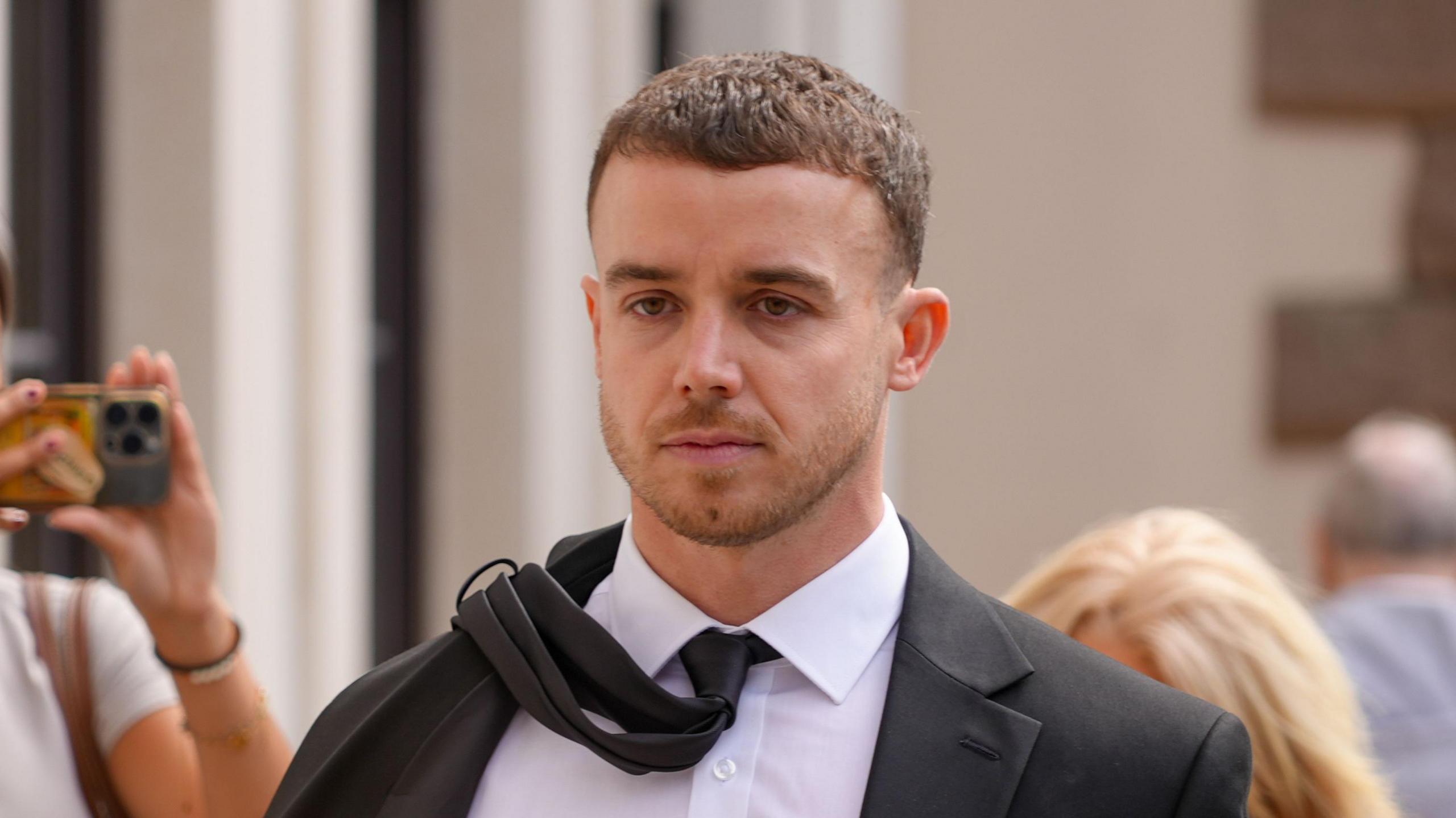 A man wearing a suit and tie walking into the royal court - his tie has flown onto his shoulder with the wind.