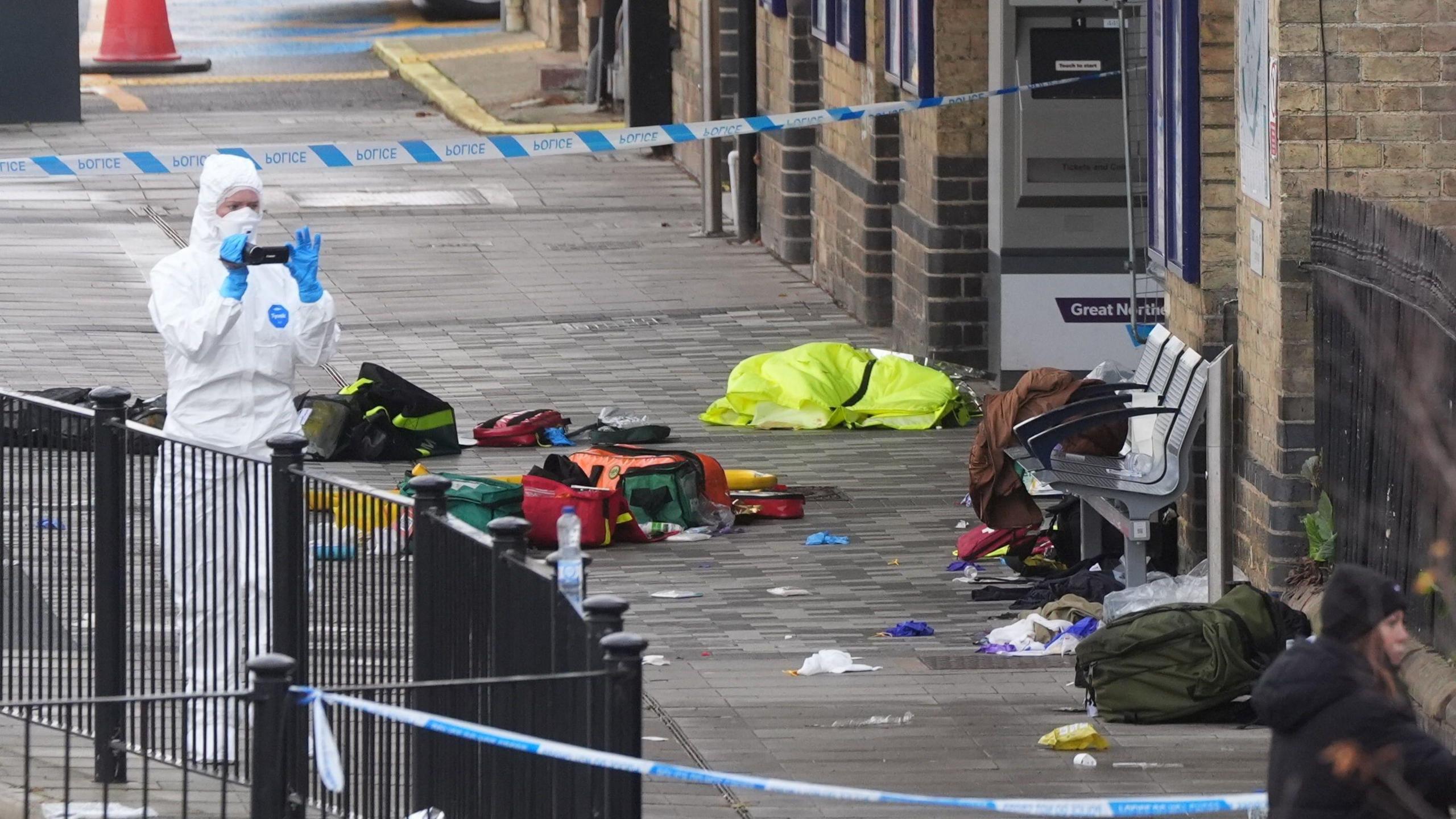 A crime scene at the station - with a blue and white police tape and a person in a white forensic suit taking pics.