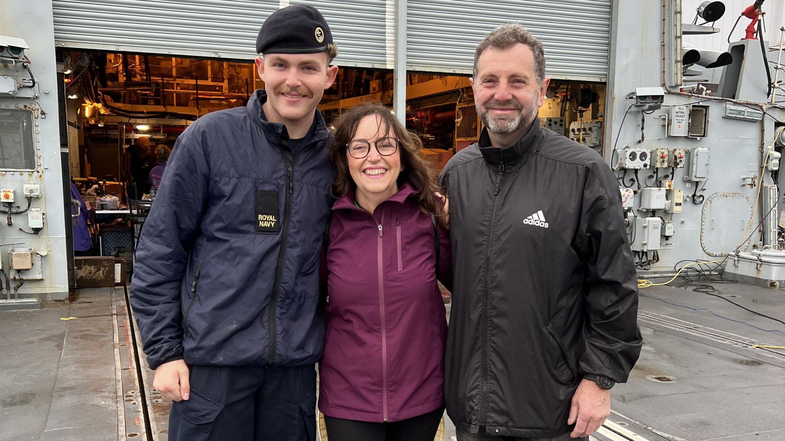 A son, his mother and father with arms around the shoulders smiling whilst standing onboard the HMS Richmond.
