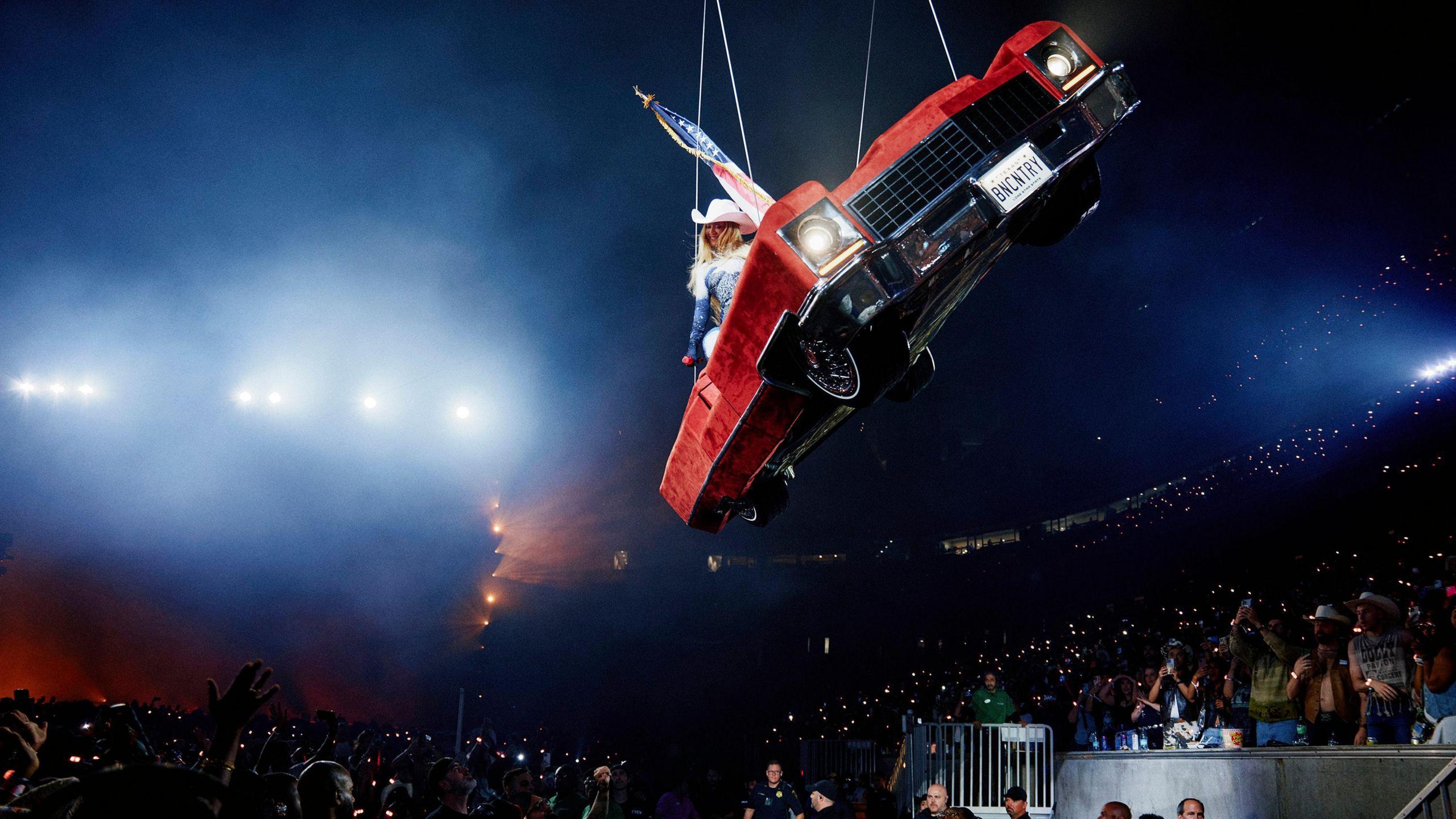 Beyonce smiles at the crowd below, while she is lowered to the ground in the red cadillac, which is on quite a tilt.