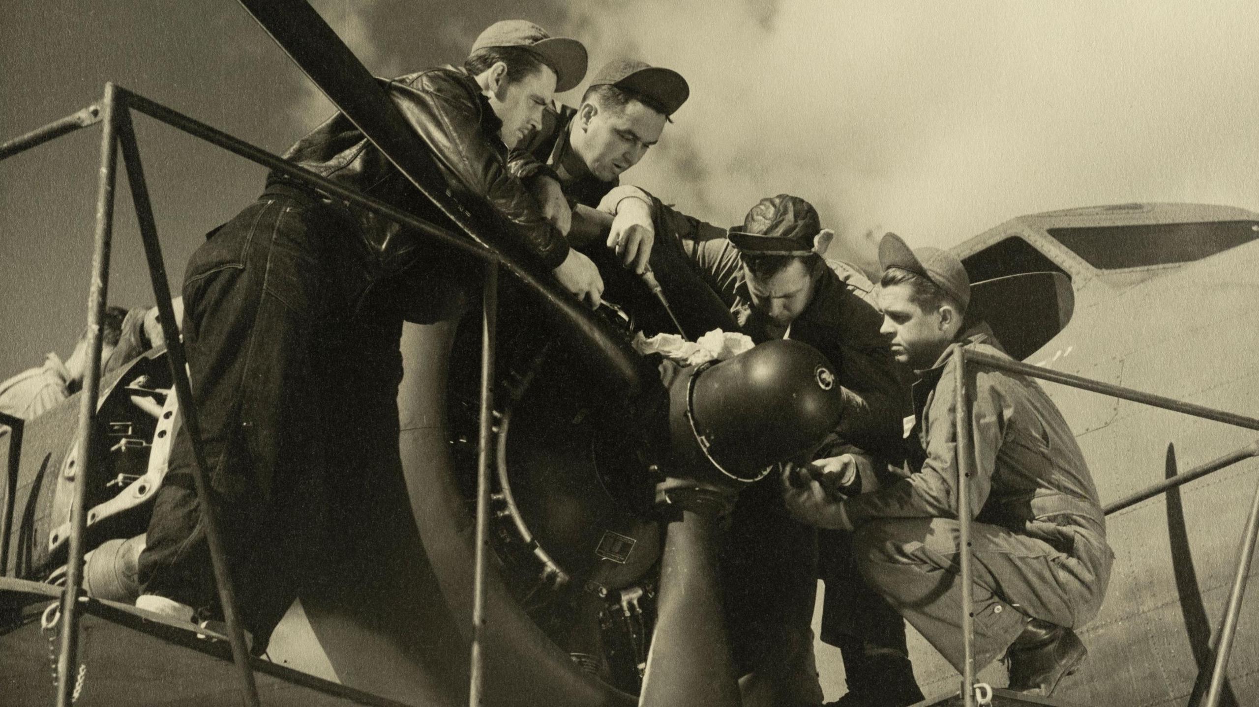 A black and white still image from a film, which shows airmen around the propeller of an aircraft.
