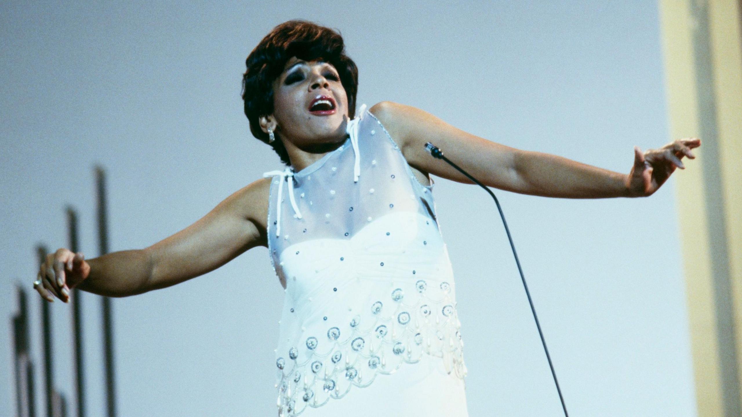 Shirley Bassey wearing a white dress on stage