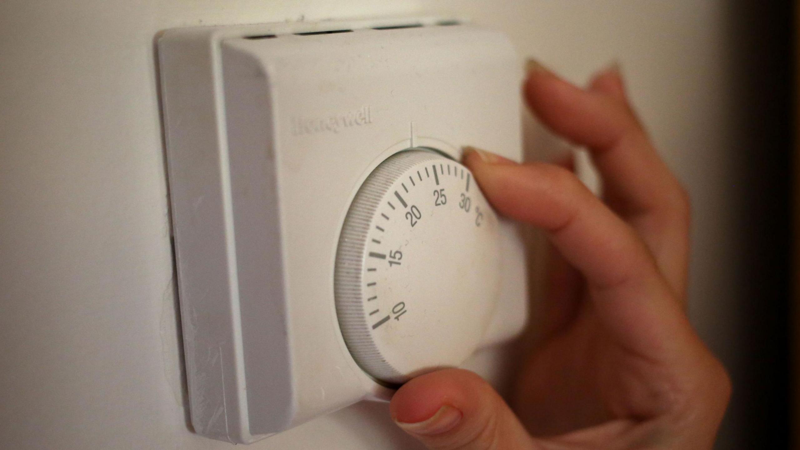 An image of a human hand, turning down a thermostat