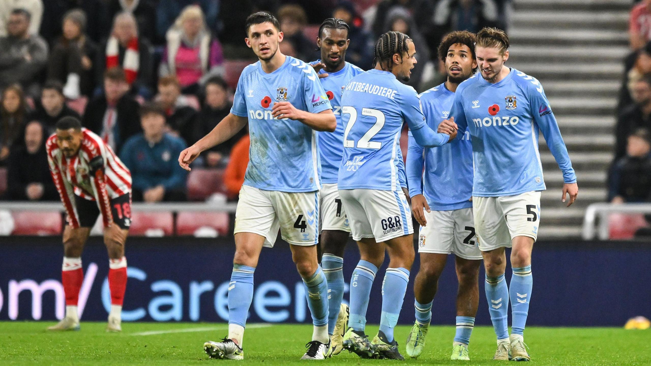 Coventry players stand together celebrating Jack Rudoni's goal against Sunderland, while Sunderland player Wilson Isidor puts his hands on his knees, his face showing disappointment