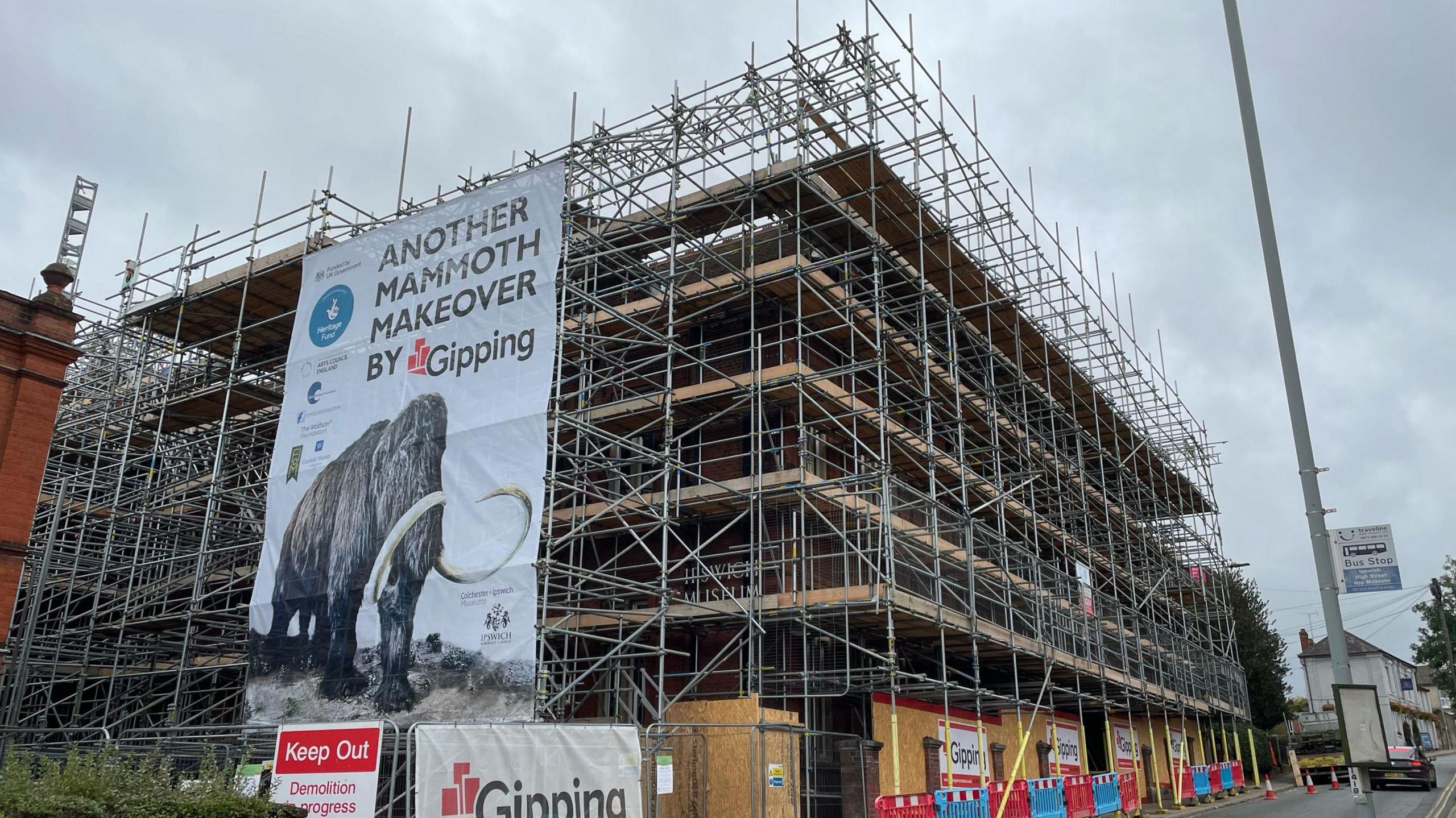 A photo of the museum's exterior. The museum is heavily covered in scaffolding from the ground to its roof. A sign has been placed over the top of the scaffolding that reads, 'Another mammoth makeover by Gipping'.