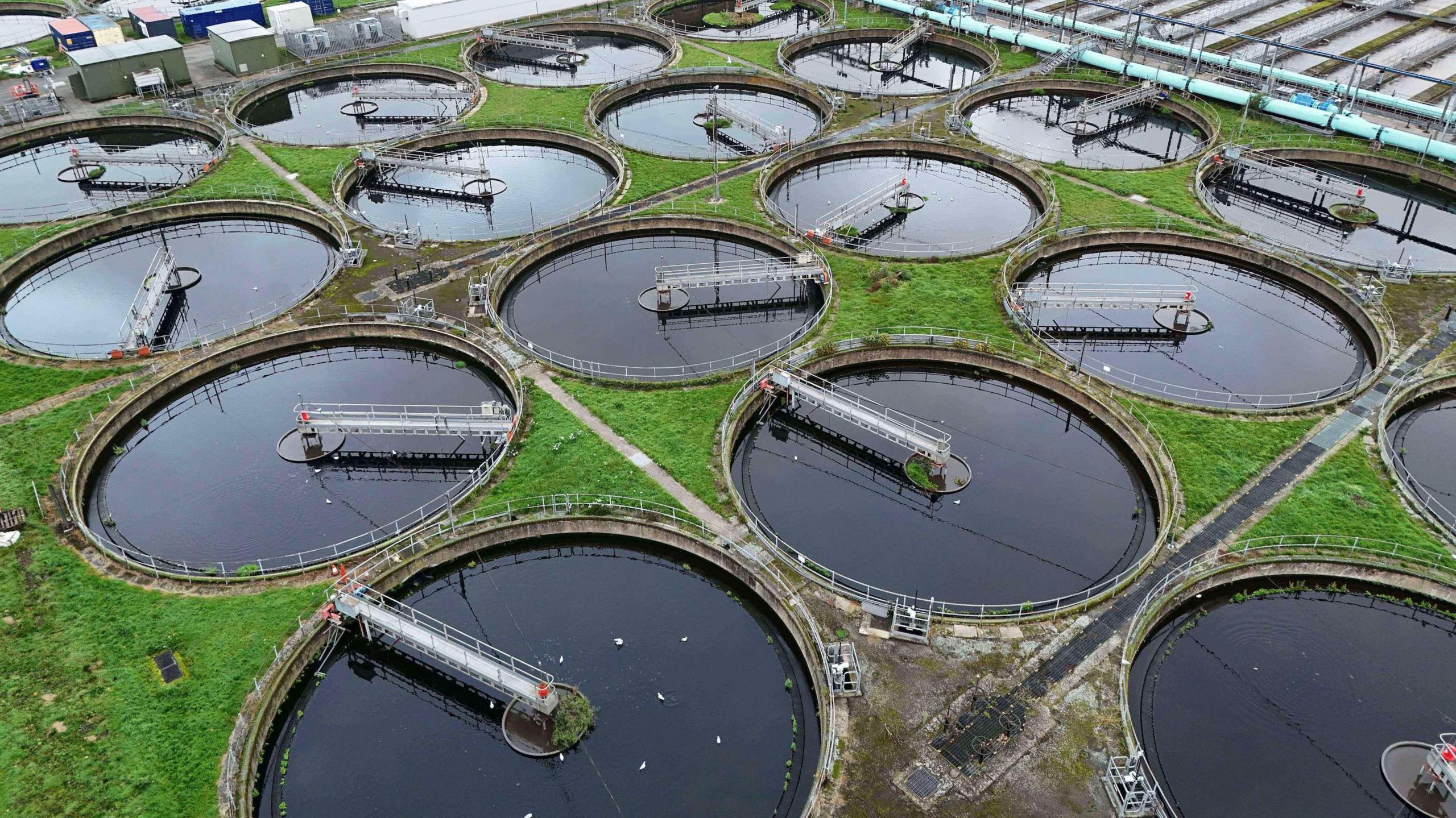A general shot of a water treatment plant. There are several circular vats of water, each with an arm stretching from the middle to the edge of the circle. In between the circles are patches of grass.