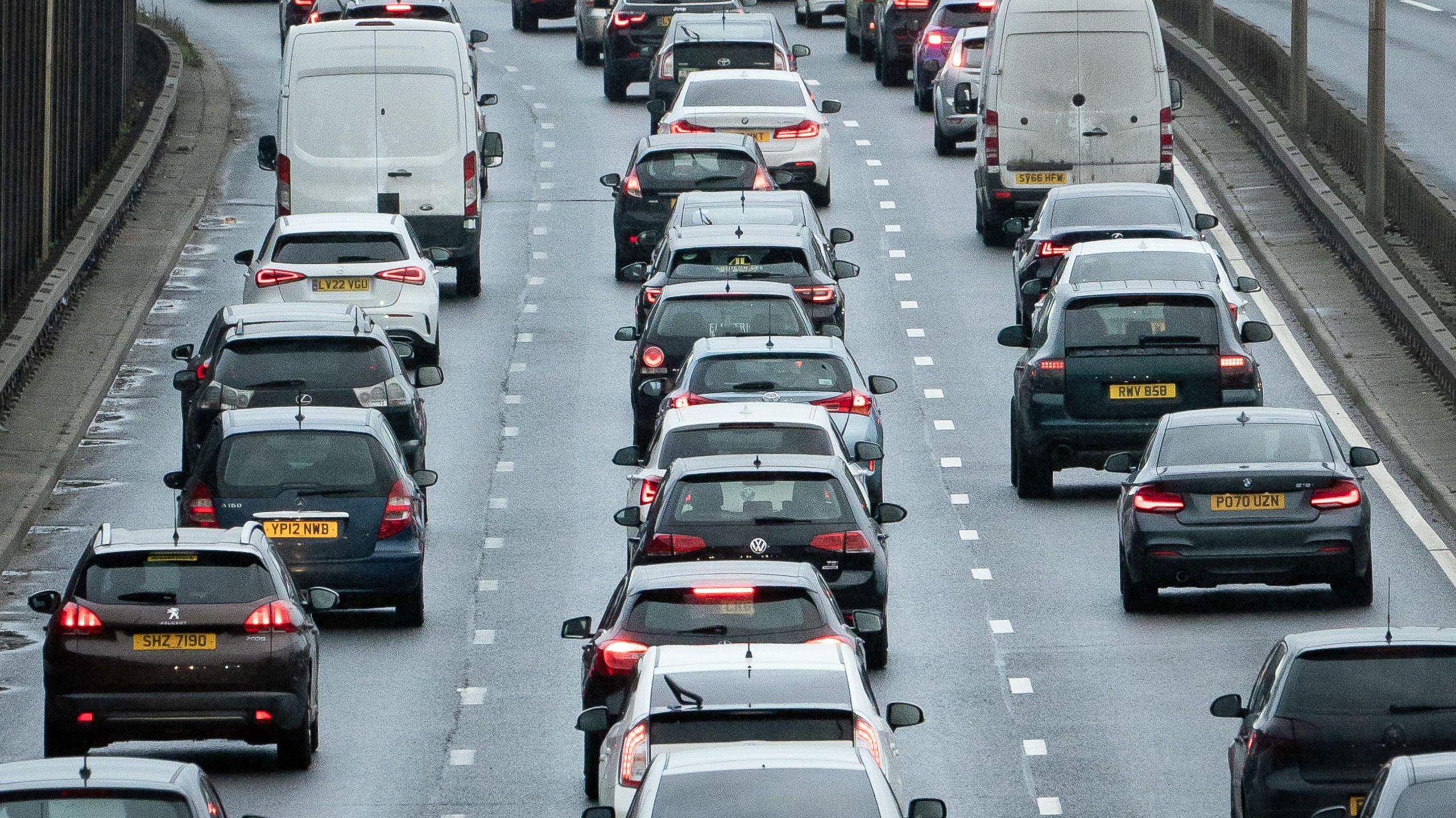 Three lanes of standstill traffic on a busy road on the A13 in England. A mix of cars and vans are on the road.