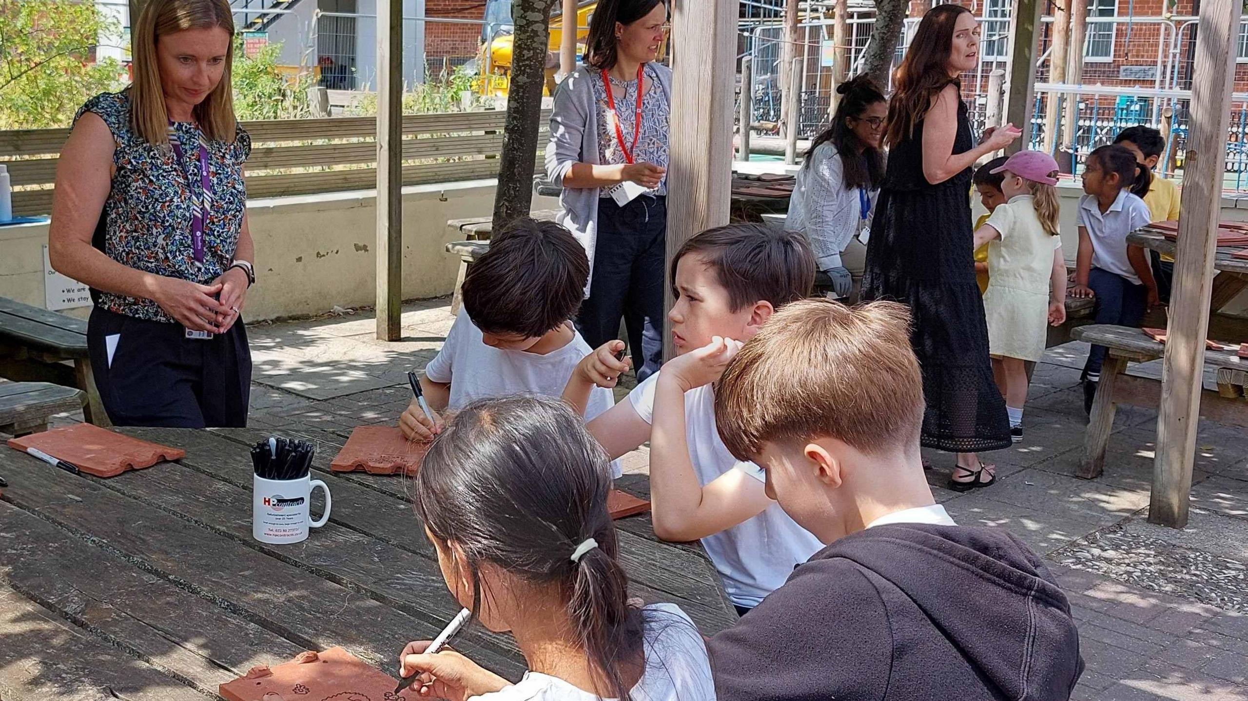 School children being supervised by teachers whilst drawing on roof tiles as part of a refurbishment project.