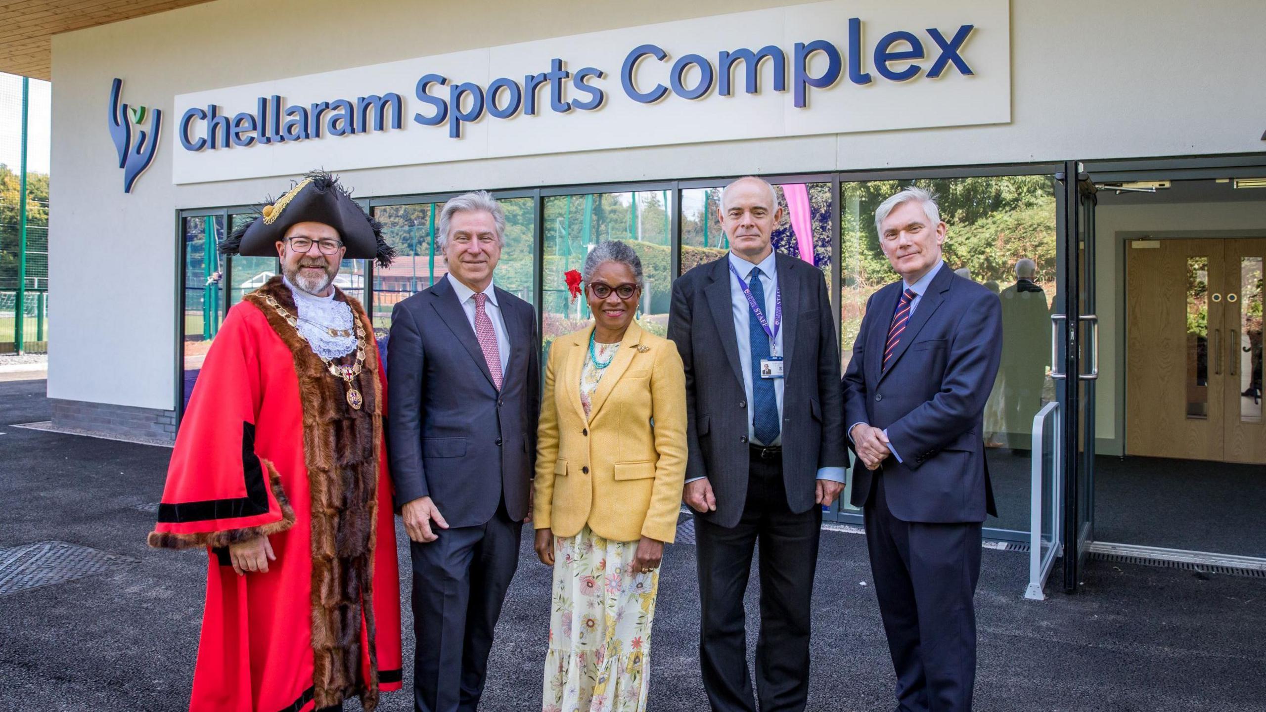 A group of people, including the mayor of Bristol, pose in front of the new Chellaram Sports Complex which is owned by Clifton College. The walls of the sports centre are cream and its name is displayed in blue letters