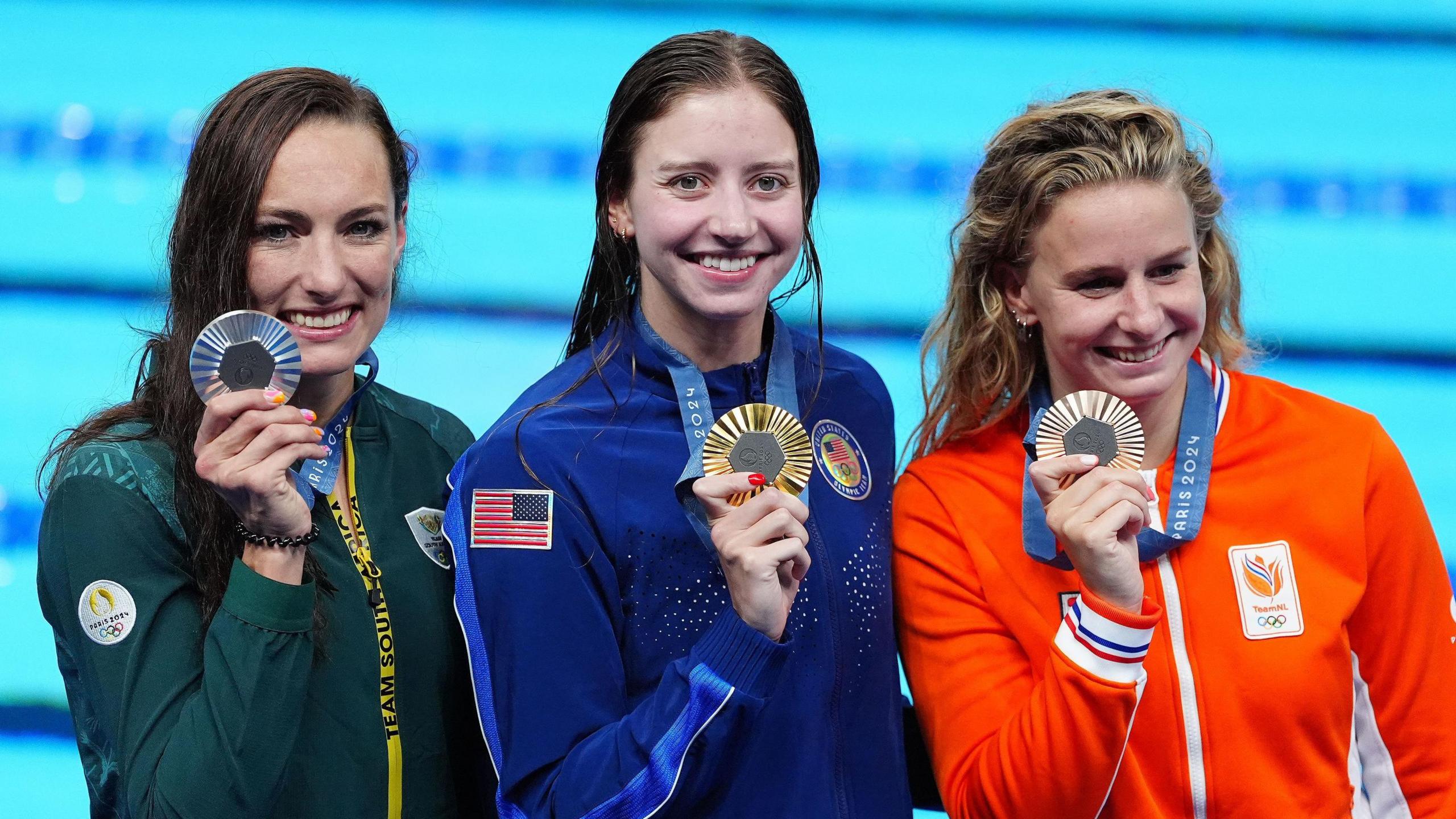 200m breaststroke medallists Tatjana Smith (left), Kate Douglass (centre) and Tess Schouten (right) all hold up their medals with the pool behind them