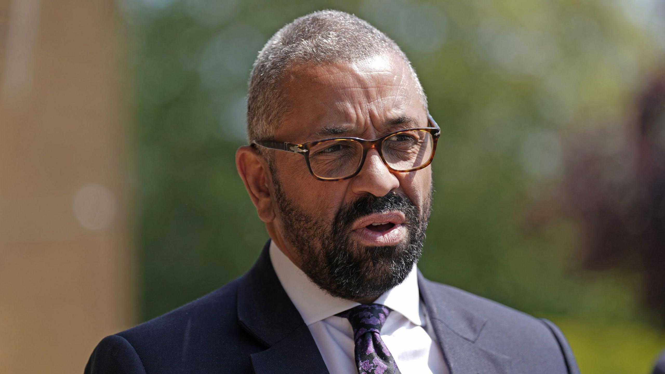 James Cleverly, who is wearing tortoise shell glasses and a suit