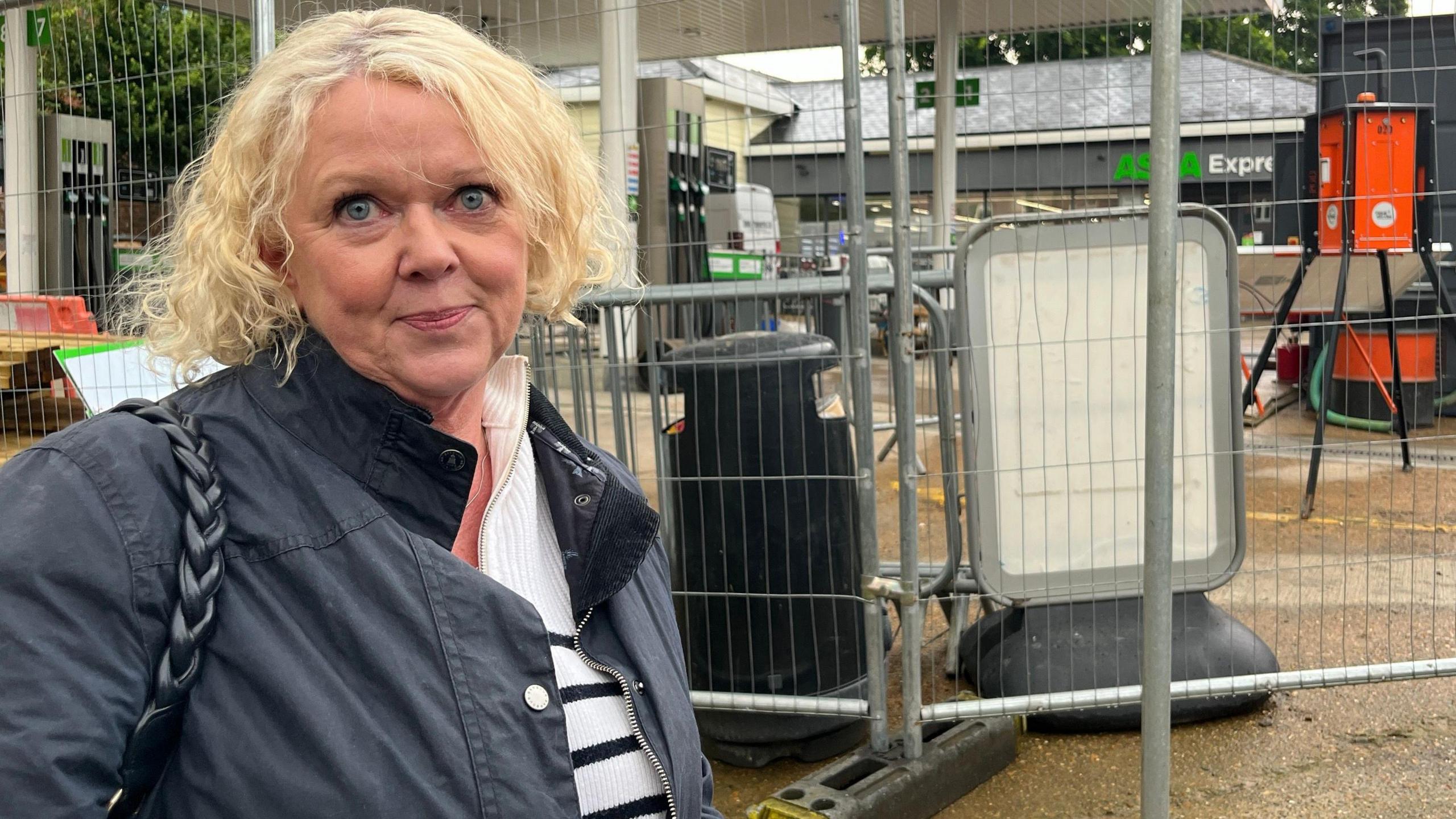 A woman with blonde hair and a black jacket stands in front of a petrol station where work was continuing